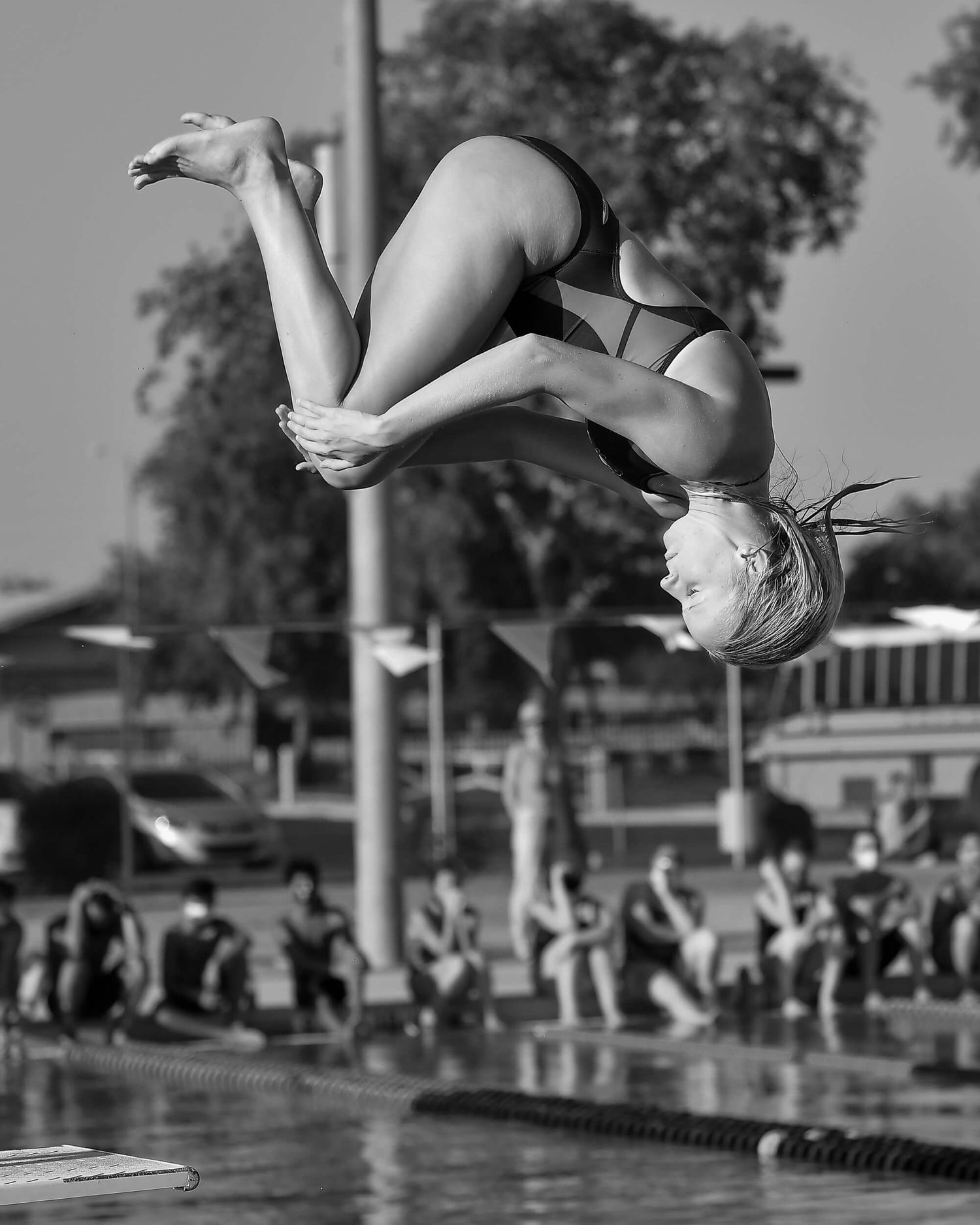 Black and white photo of a female diver performing a backflip at an outdoor pool.