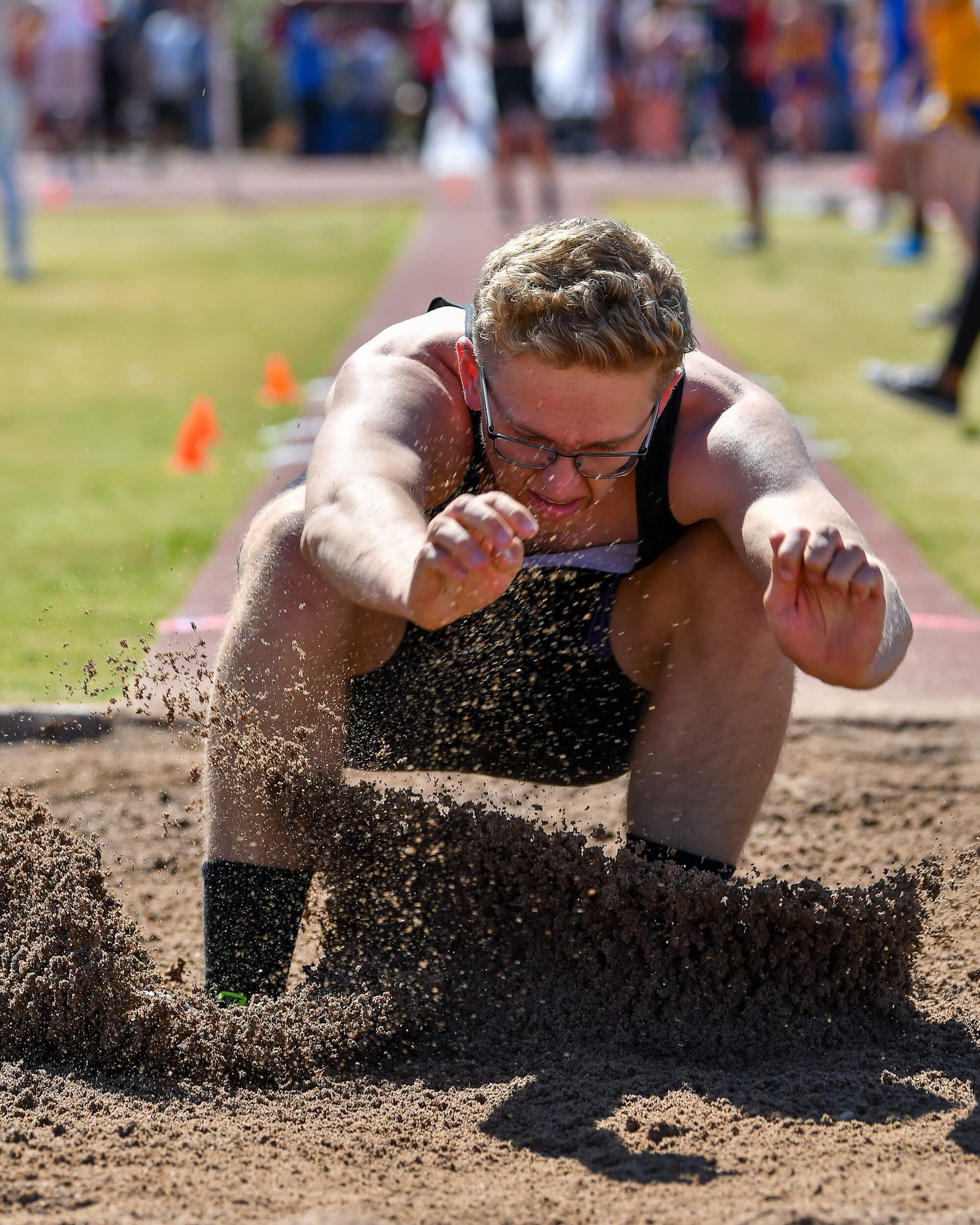 Athlete lands in sand pit during long jump competition at outdoor track and field meet.