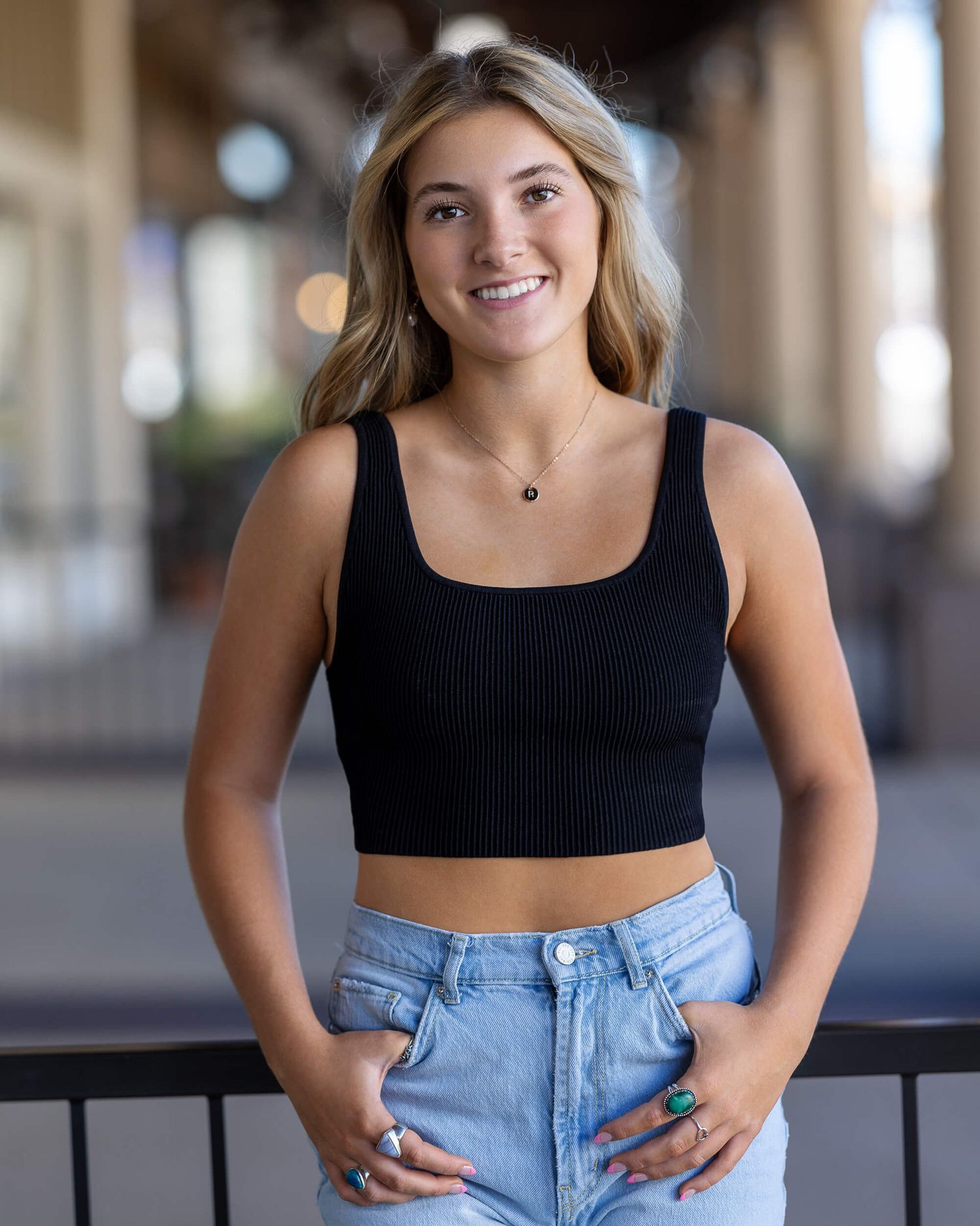 Young woman smiling in black crop top and jeans posing outdoors.