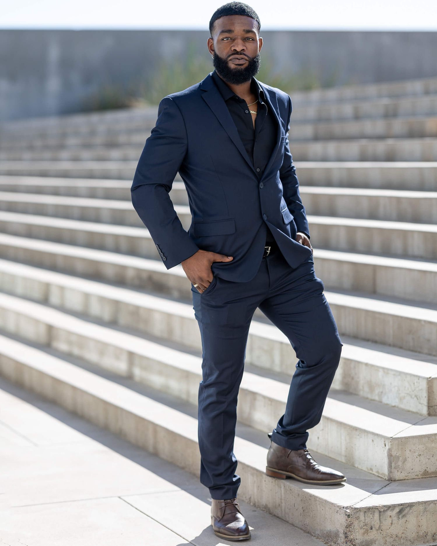 Stylish man in navy suit posing on outdoor steps wearing brown leather shoes.