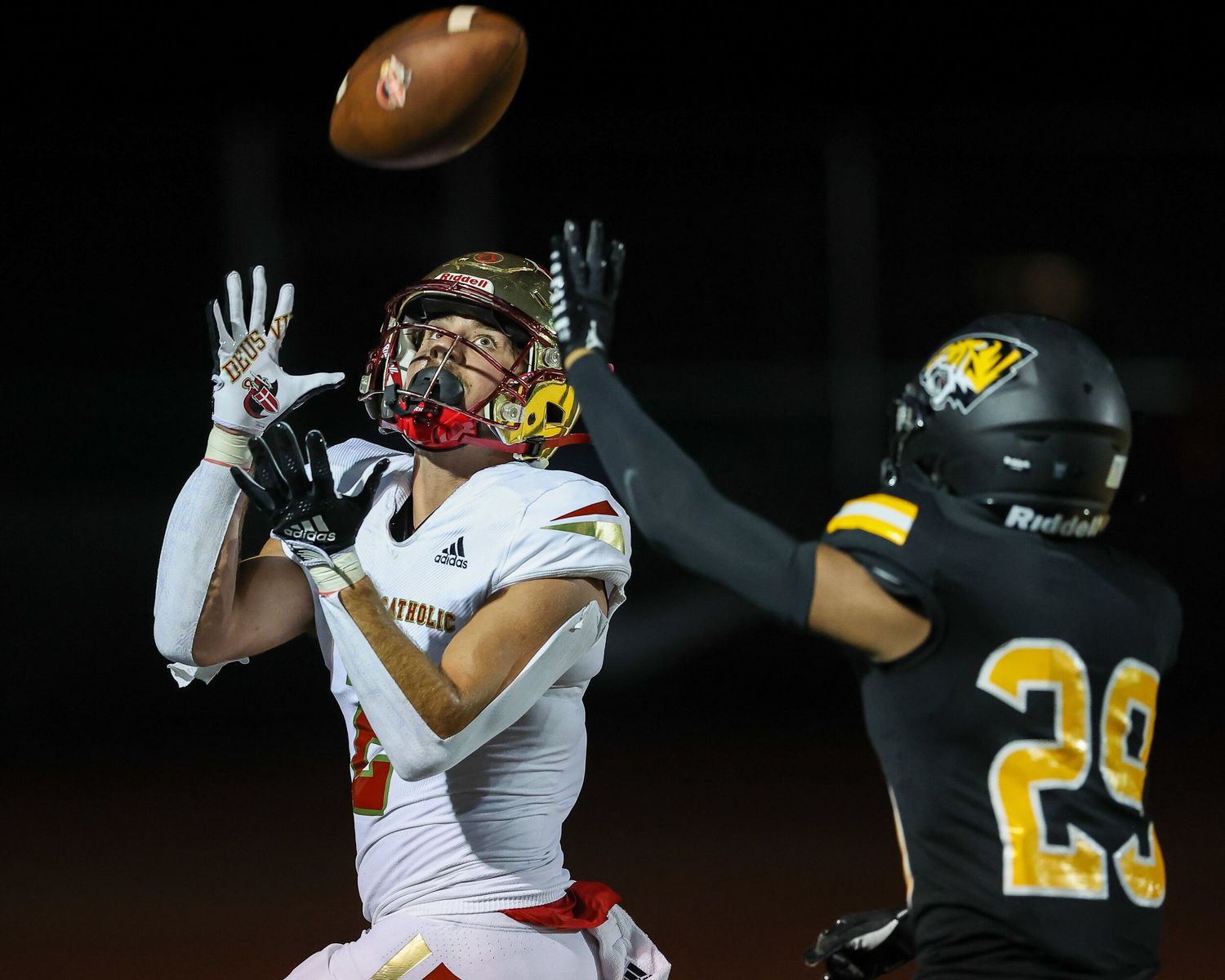 High school wide receiver catches a football while being defended during a night game.