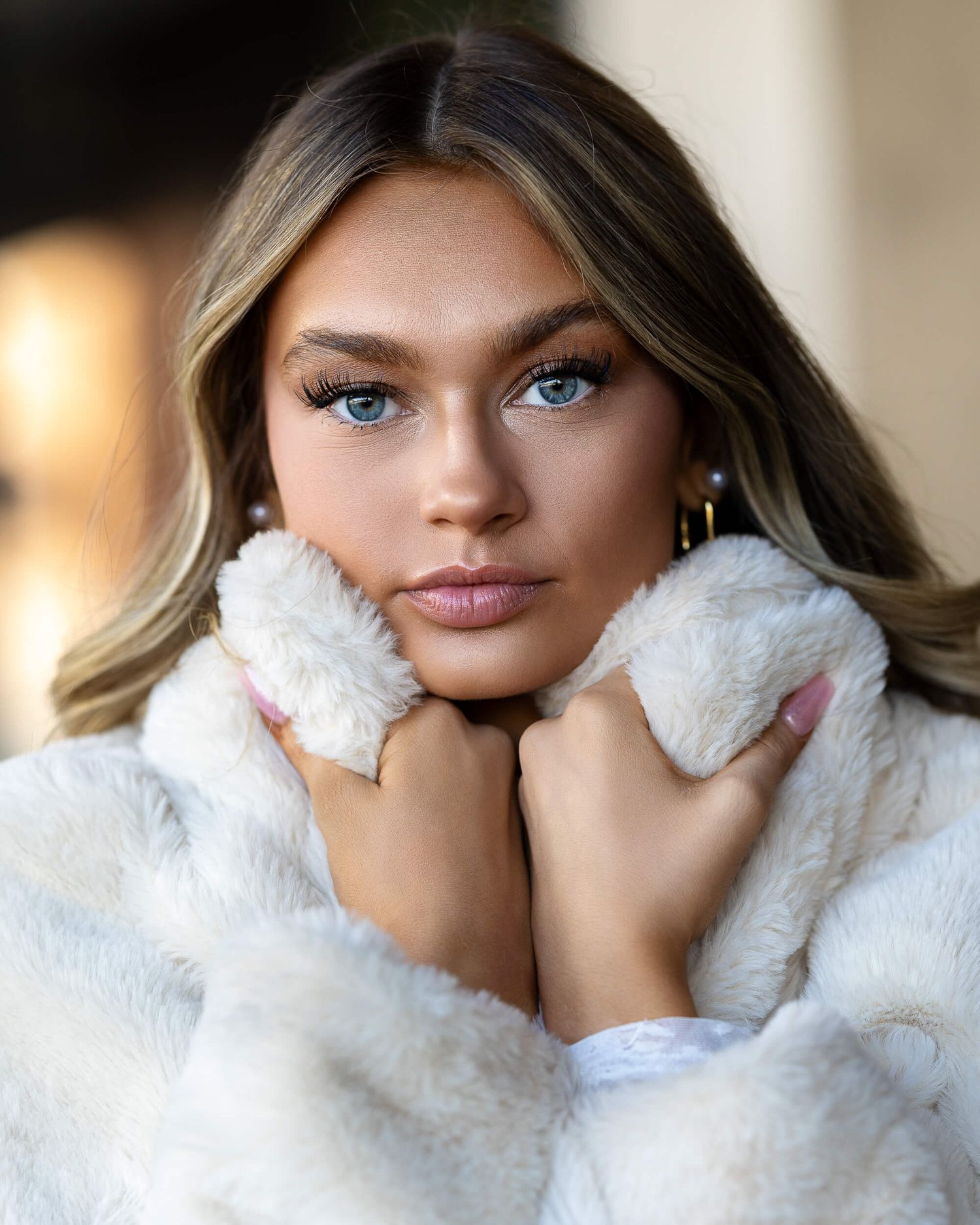 Young woman with blue eyes in white fluffy coat holding collar up to her face.