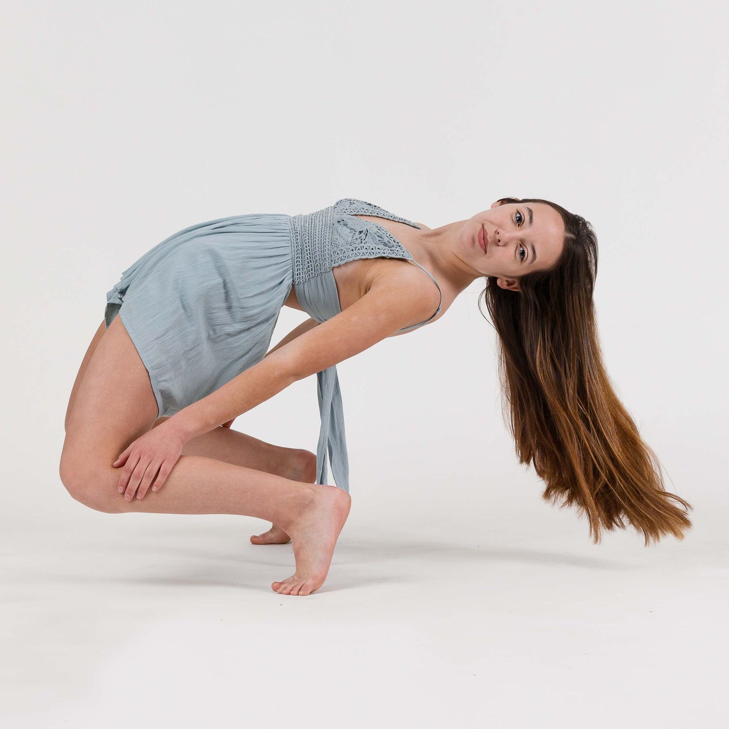 Contemporary dancer crouches in a backbend pose wearing a gray outfit on a clean white studio background.