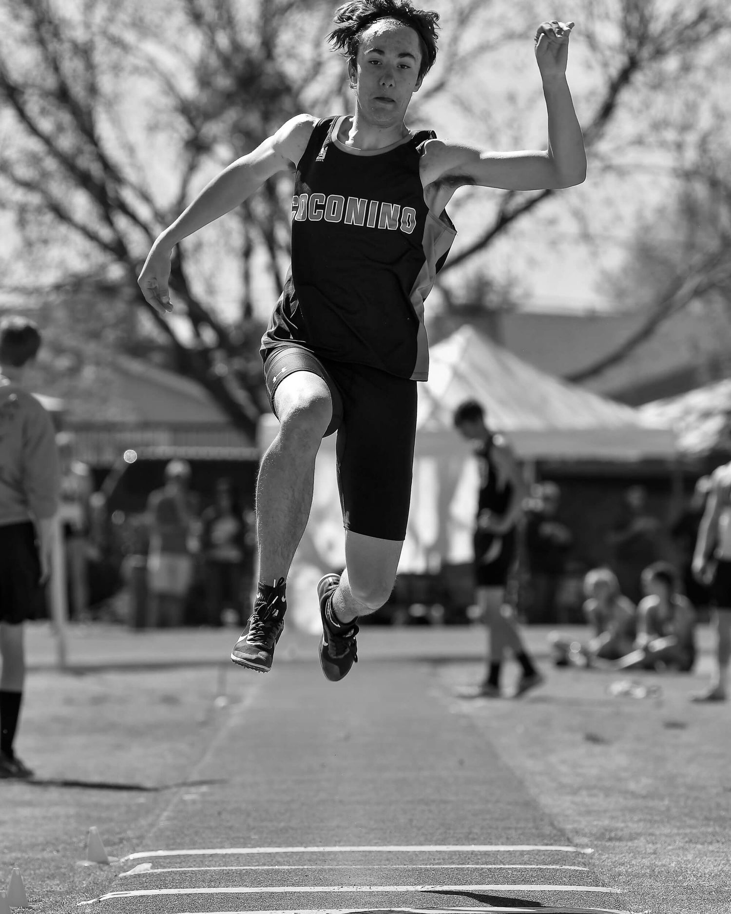 Male track athlete performs a long jump during an outdoor competition in black and white photo.
