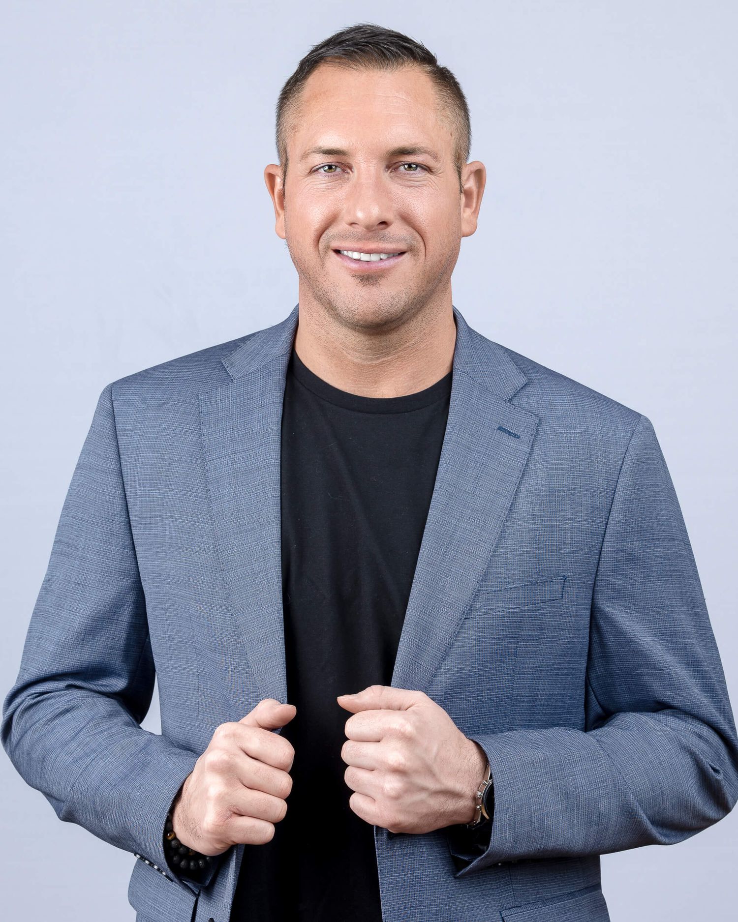 Professional man in blue blazer and black shirt smiles confidently for a corporate headshot photo.