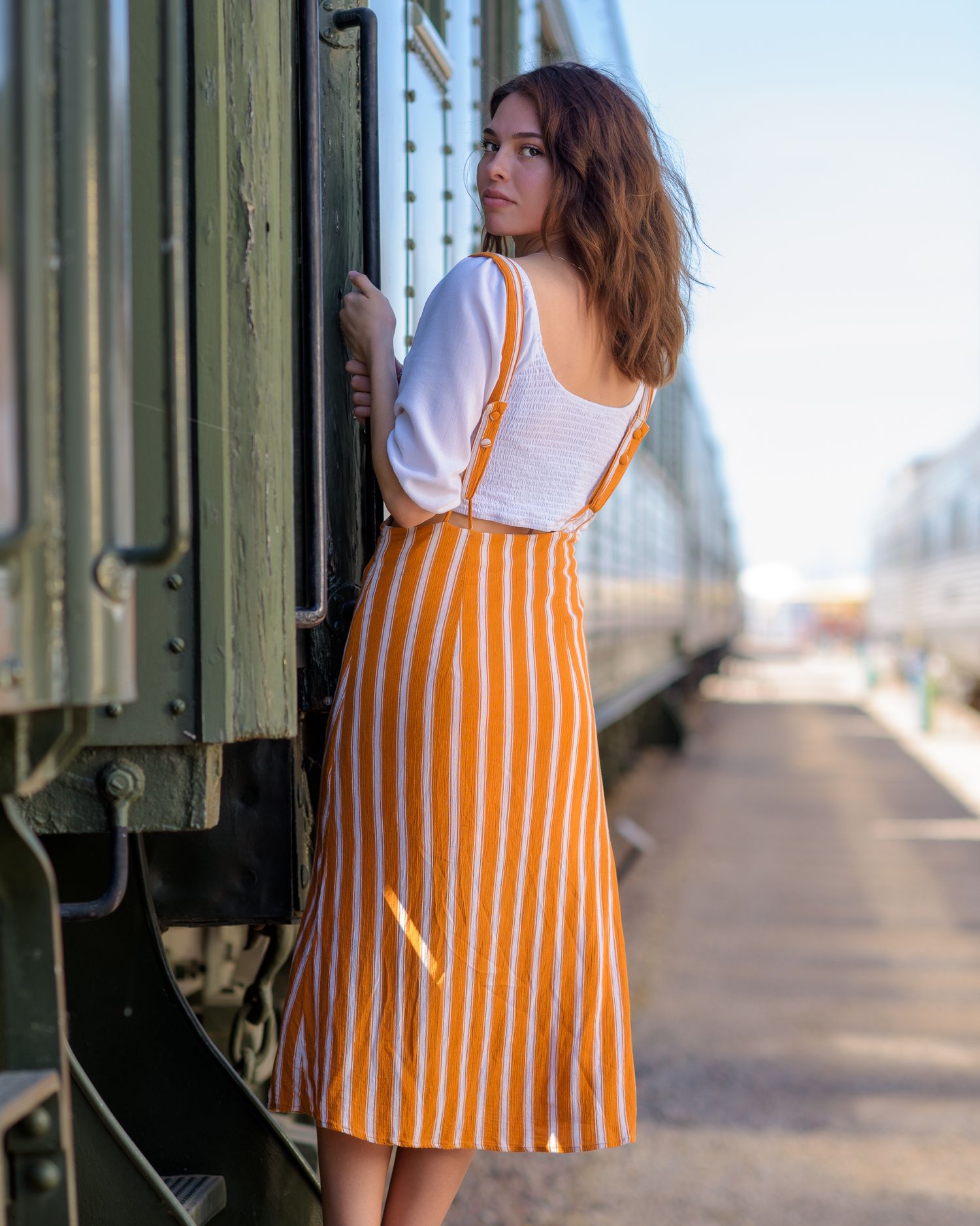 Young woman in striped orange skirt and white top boards vintage train at station.