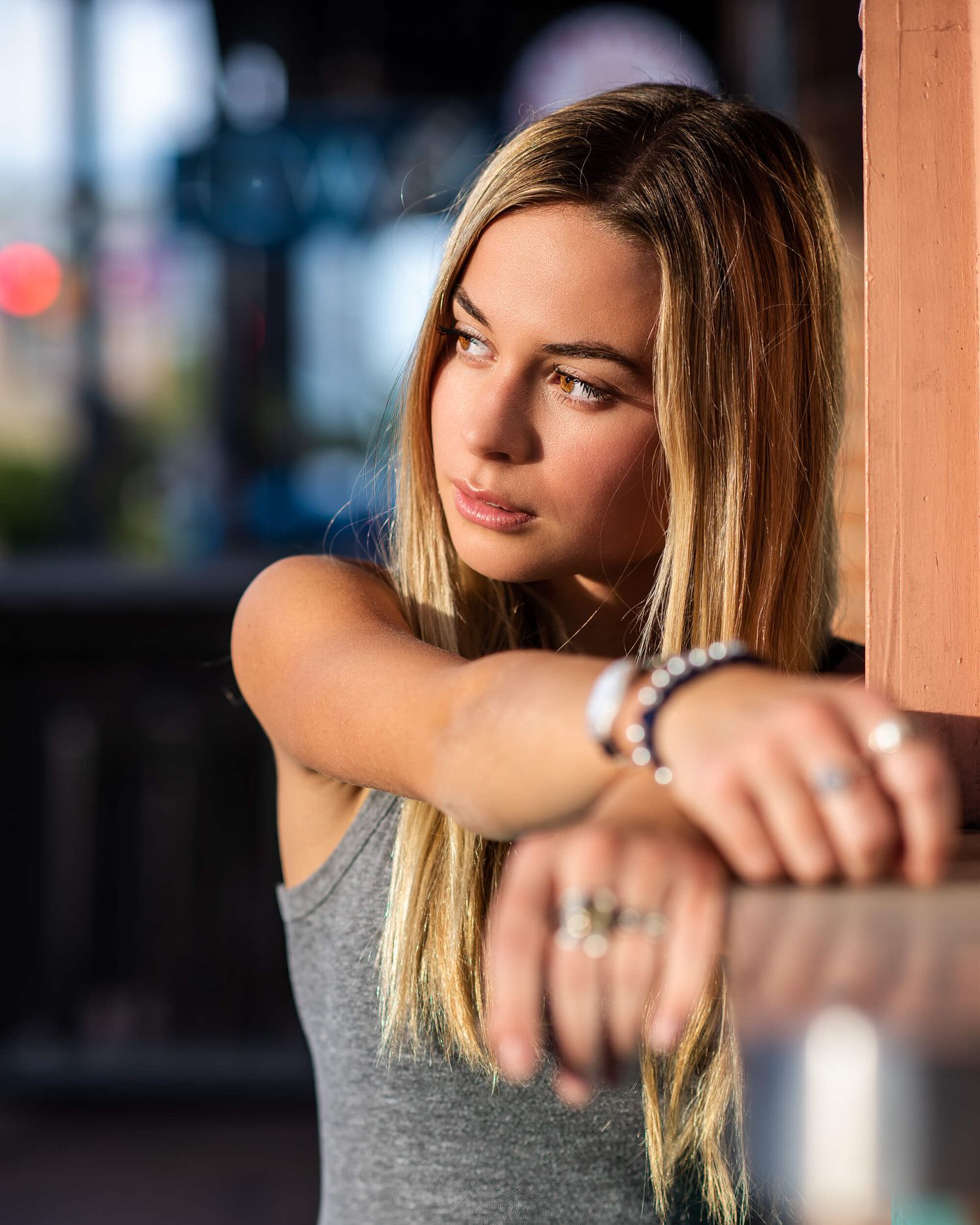 Young blonde woman leaning on wooden surface in gray tank top.