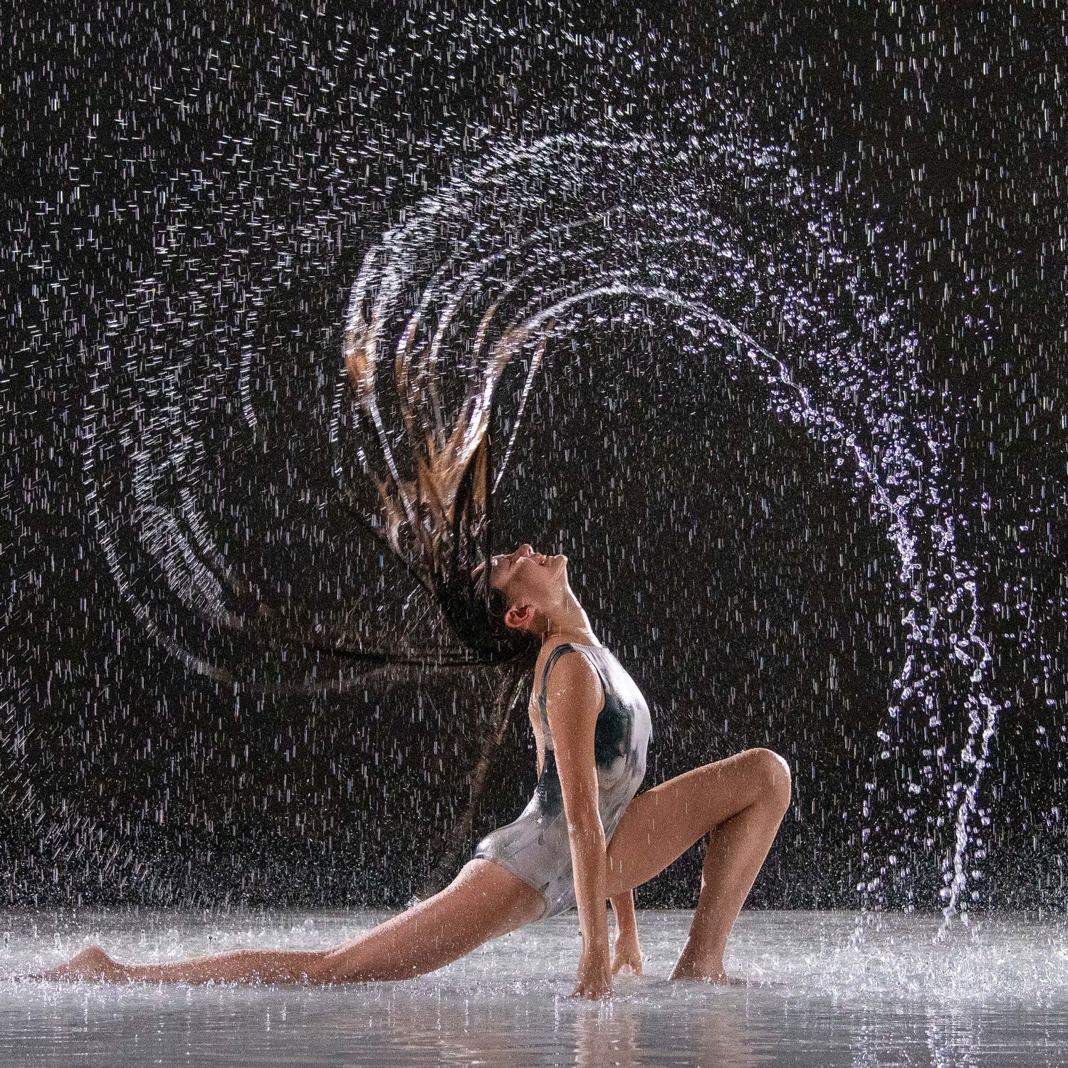 Dynamic dancer flipping wet hair creating a water arc splash against dark background.