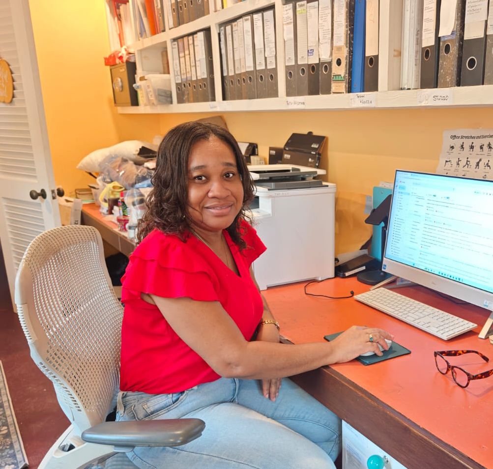 Woman in red top smiling at desk with computer, keyboard, and bookshelves in organized home office.
