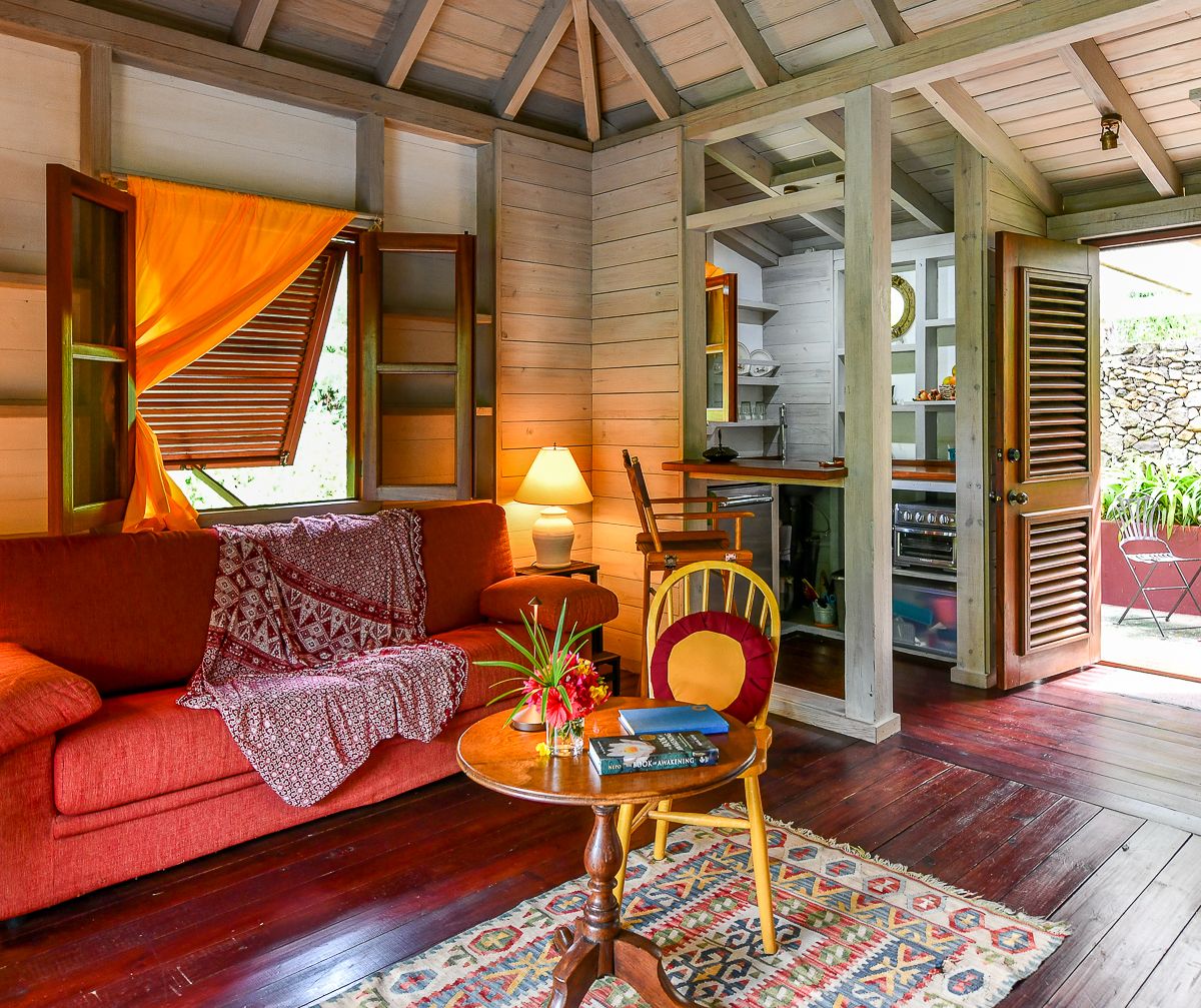 Charming Caribbean cottage interior with red sofa, hardwood floors, vaulted ceiling, and open kitchen bathed in warm light.