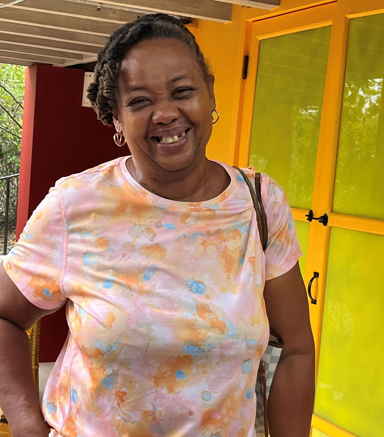 Smiling woman in colorful floral t-shirt standing outdoors near bright yellow cabinet doors.