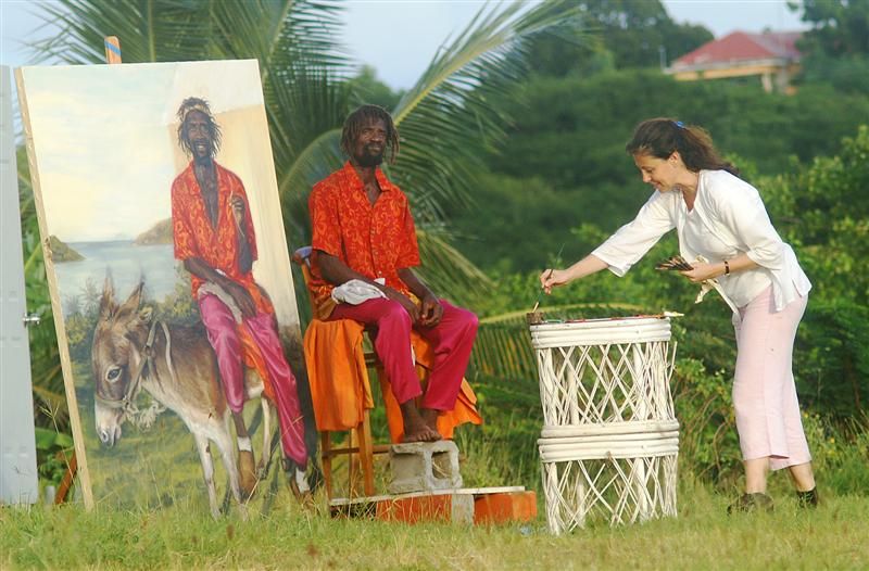Artist painting portrait of local man seated outdoors beside large canvas in tropical garden setting.
