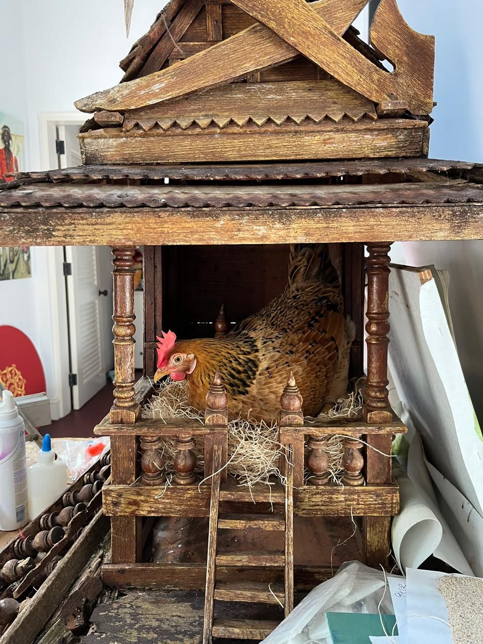 A golden hen nesting inside an ornate carved wooden birdhouse with a small ladder.