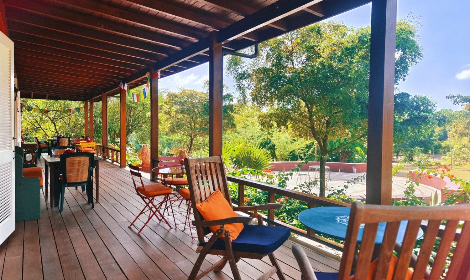 Spacious wooden deck with dining chairs and lush green tropical garden views on a sunny day.