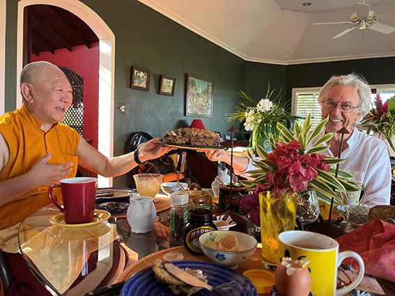 Two elderly people share a meal at a table with flowers, coffee cups, and food in a cozy dining room.