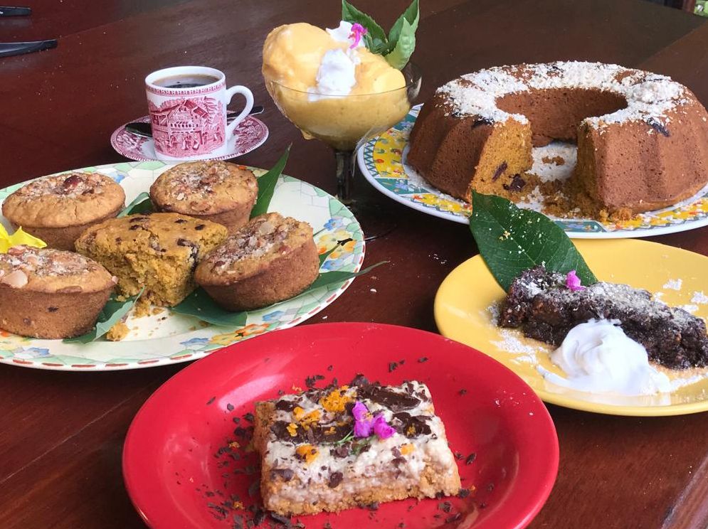 Assorted homemade cakes and muffins displayed on colorful plates on a wooden table, including a bundt cake and fruit desserts.
