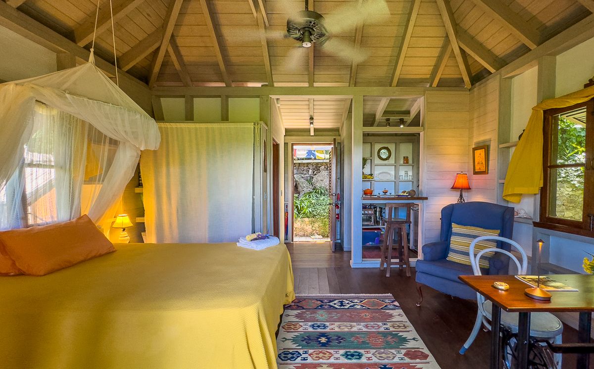 Charming cottage bedroom with canopy bed, yellow walls, vaulted wood ceiling, and tropical decor.