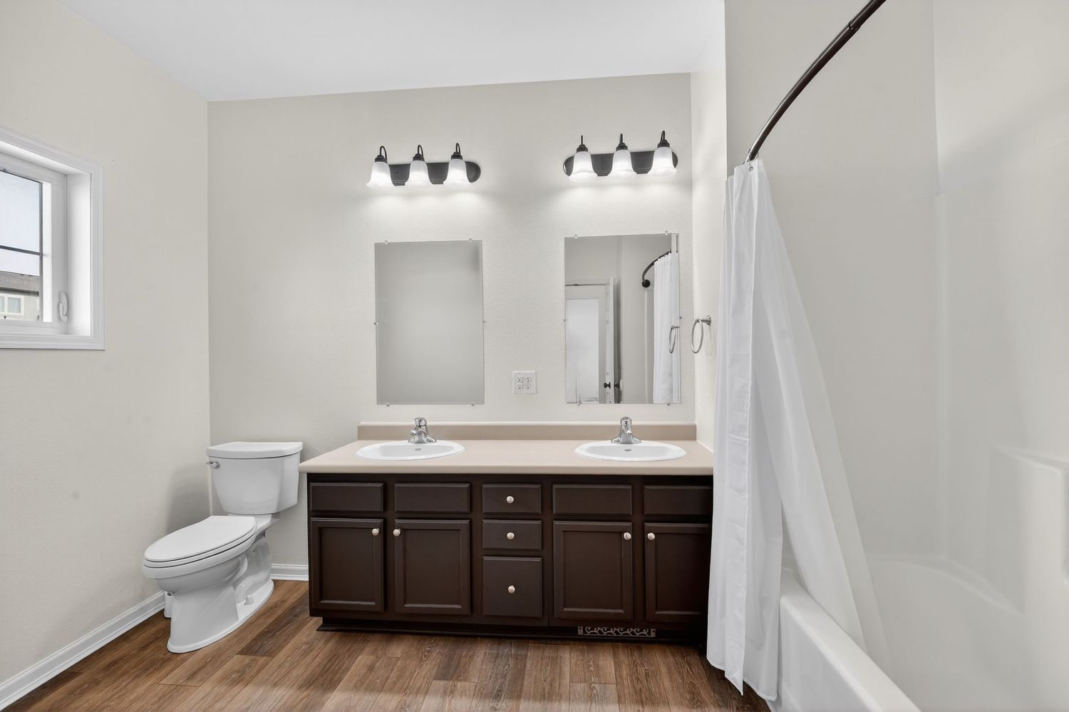 Modern bathroom with dark wood double vanity, dual mirrors, white tub with curtain, and hardwood floors.