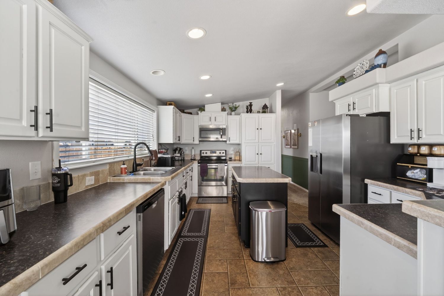 Spacious kitchen with white cabinets, dark granite countertops, stainless steel appliances, and a center island with tile flooring.