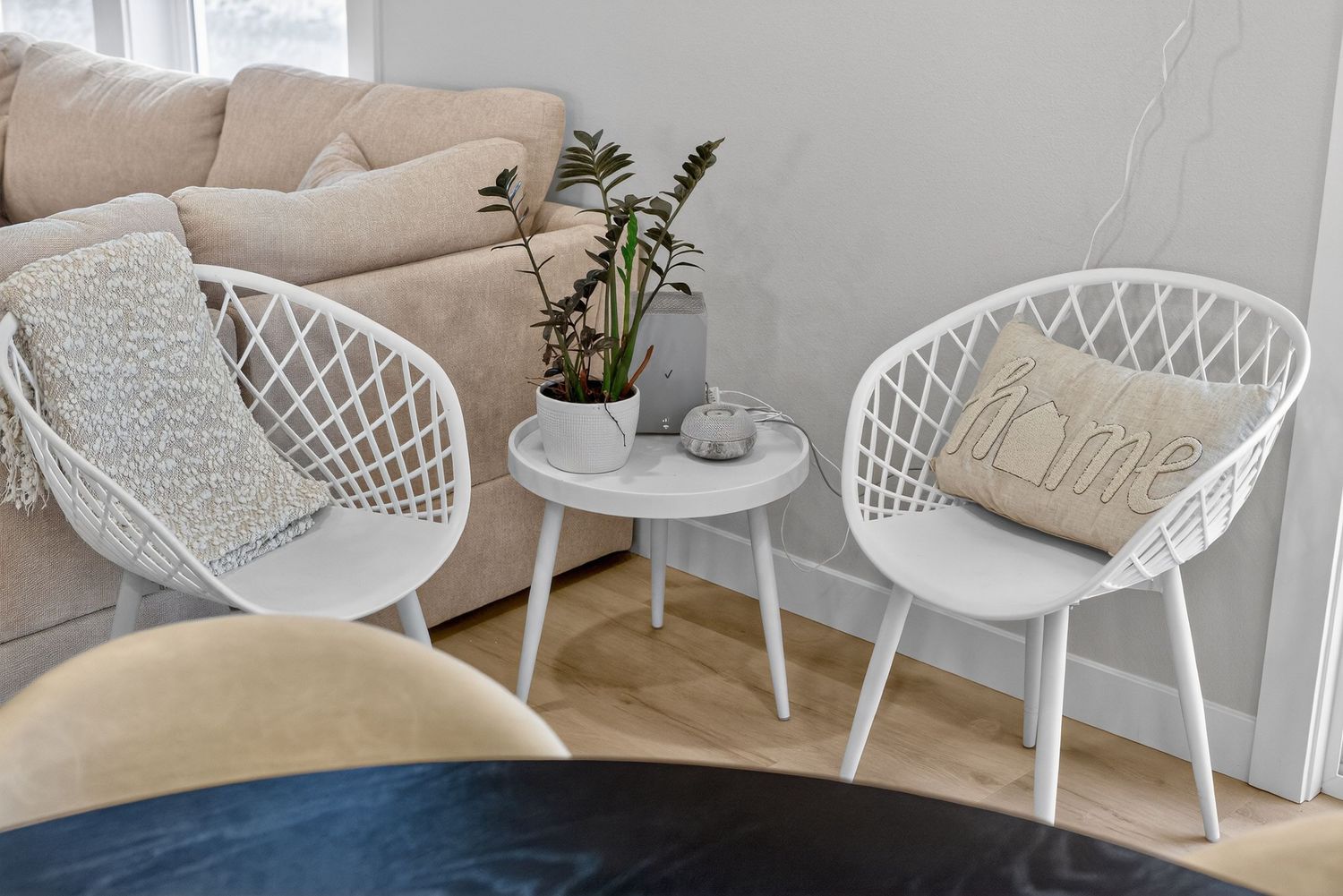 Cozy sitting area with two white wicker chairs, small round table, and potted plant.