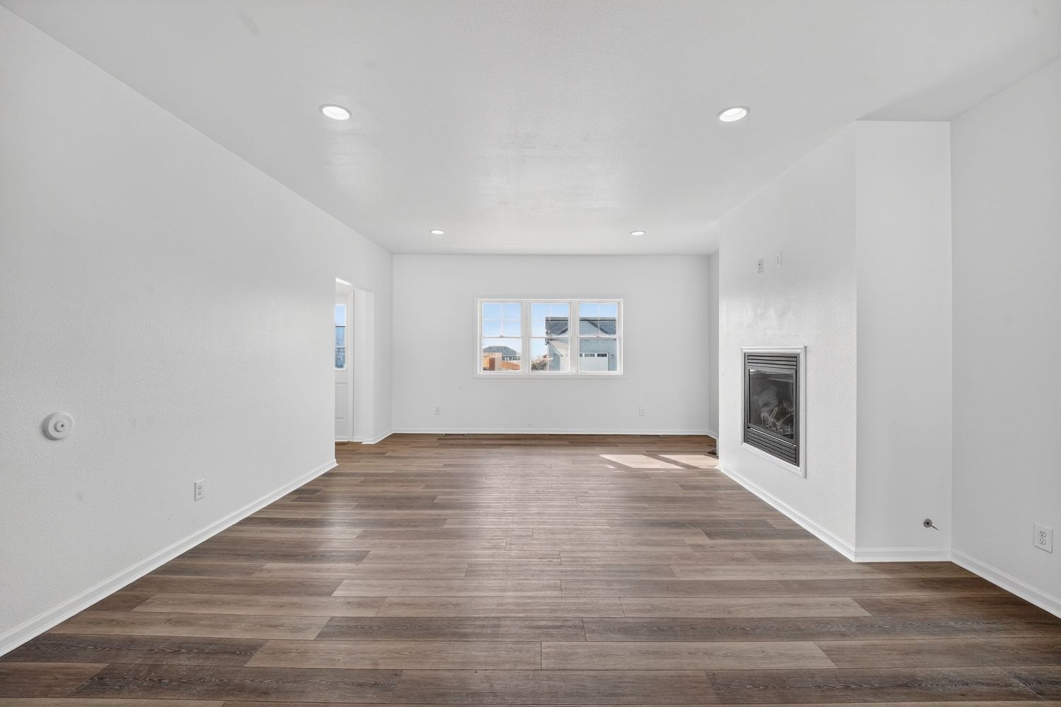 Open living room with dark hardwood floors, recessed lighting, and white brick fireplace.