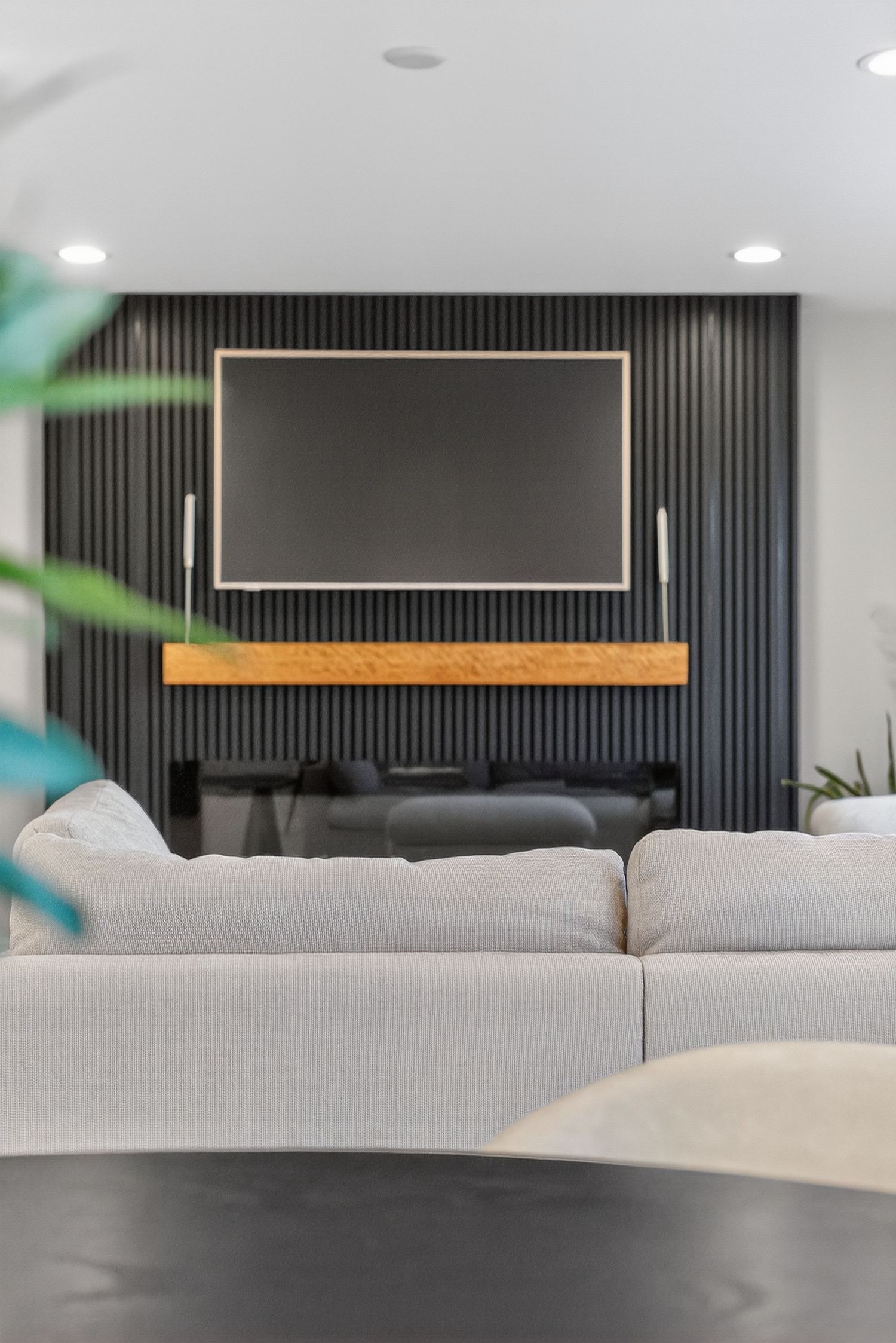 Modern living room with large sectional sofa, wall-mounted TV, and dark slat accent wall.