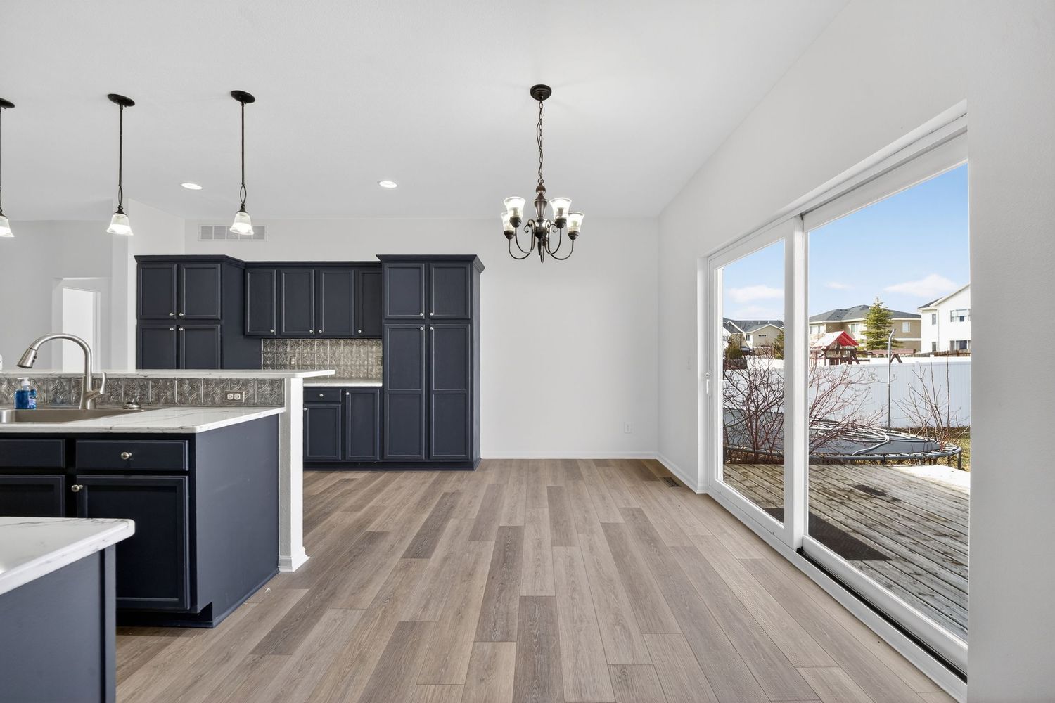 Kitchen with navy cabinets, vaulted ceiling, pendant lights, and sliding glass door.