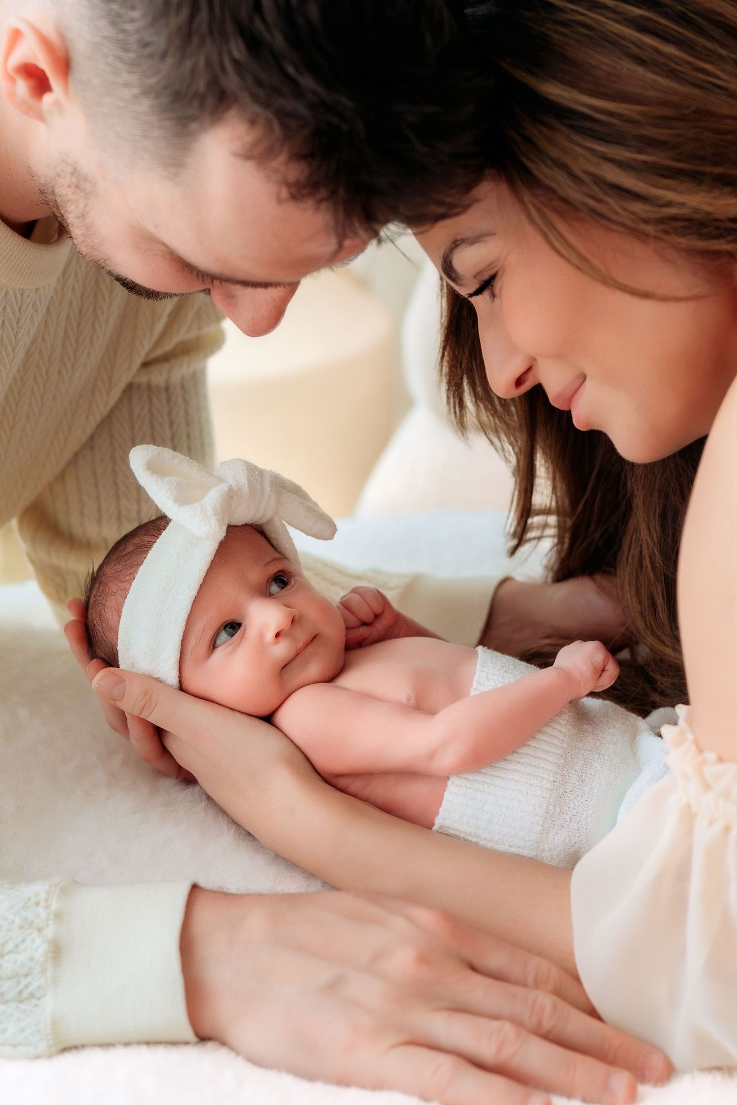 Loving parents tenderly holding their newborn baby with white bow headband together.