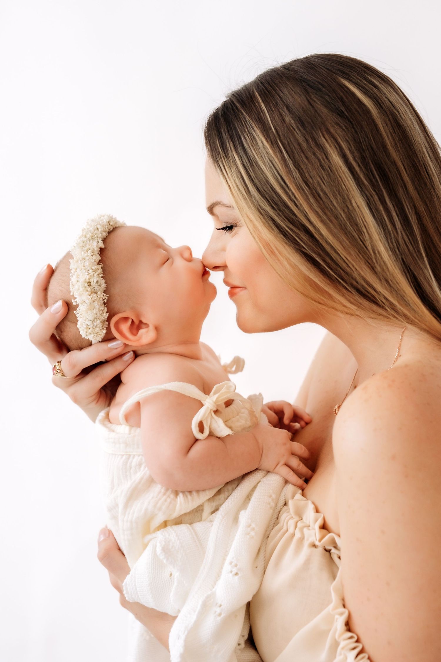 Young mother sharing a tender nose-to-nose moment with her newborn in a cream floral bonnet.