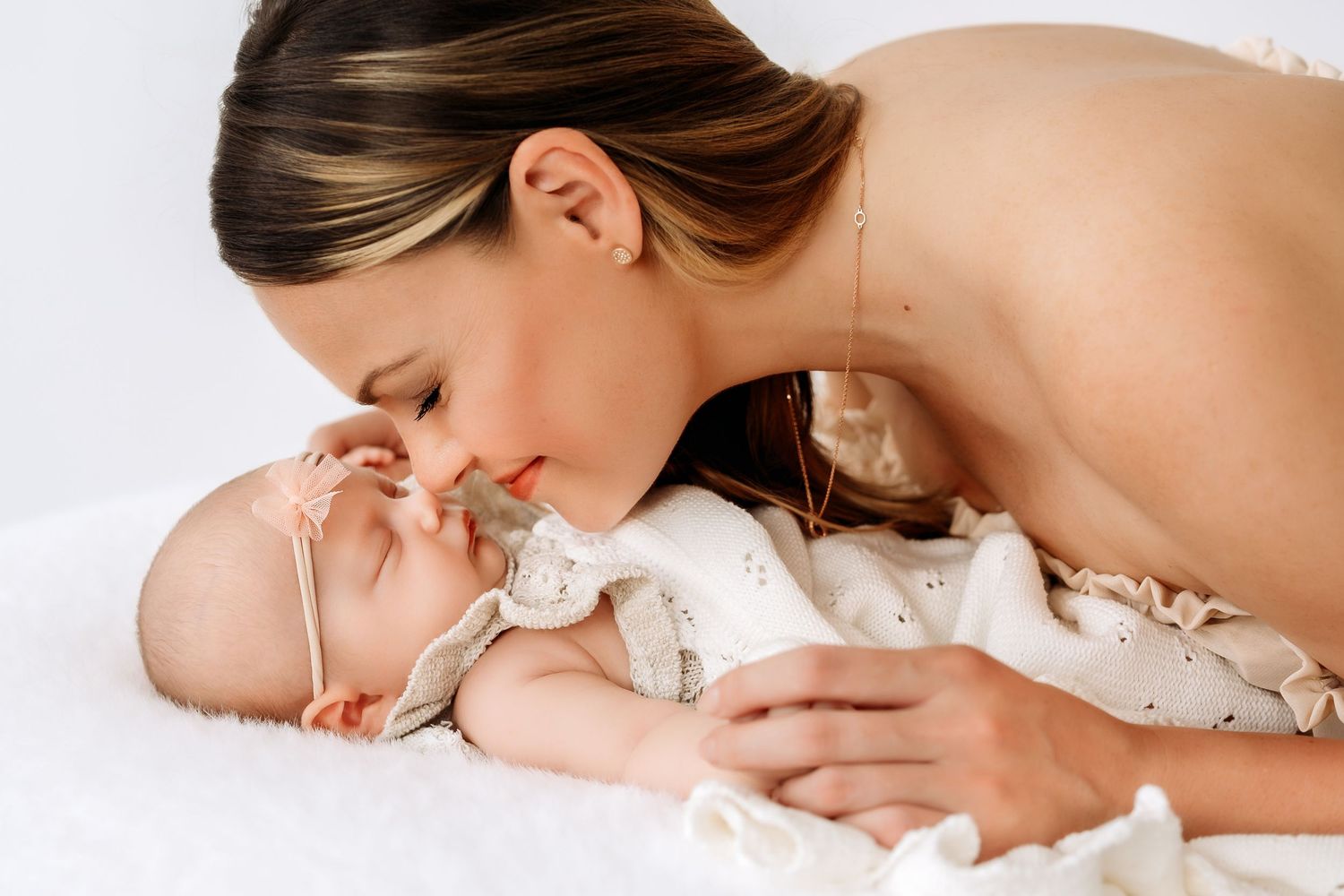Tender moment of mother kissing sleeping newborn baby girl wearing a pink headband.