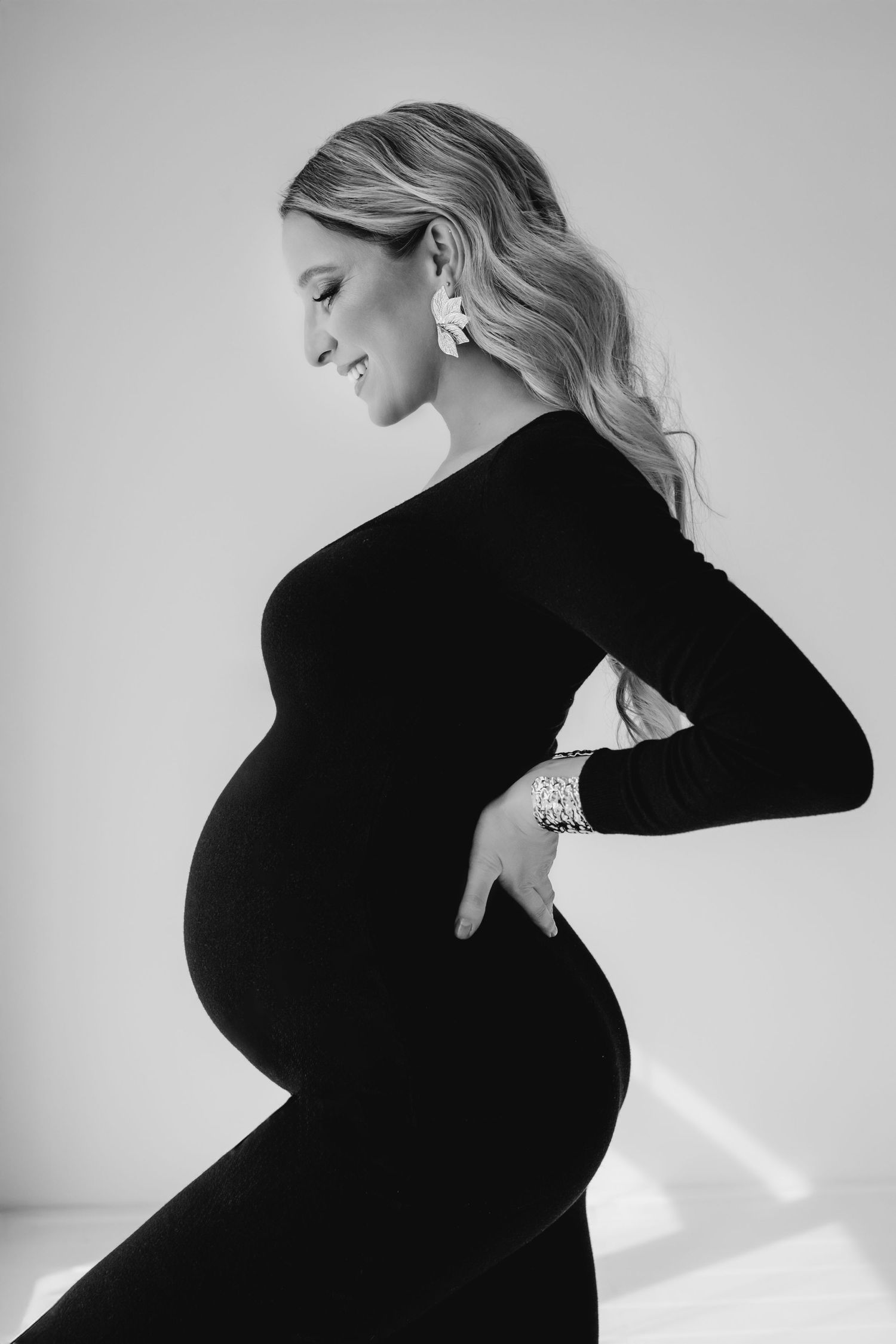 Black and white profile portrait of pregnant woman in fitted black dress showcasing baby bump elegantly.