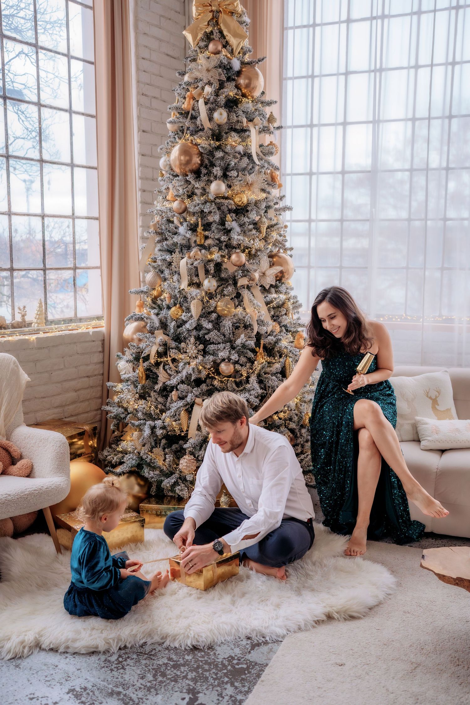 Family celebrating Christmas together near a decorated gold and white tree, opening gifts on a cozy fur rug.