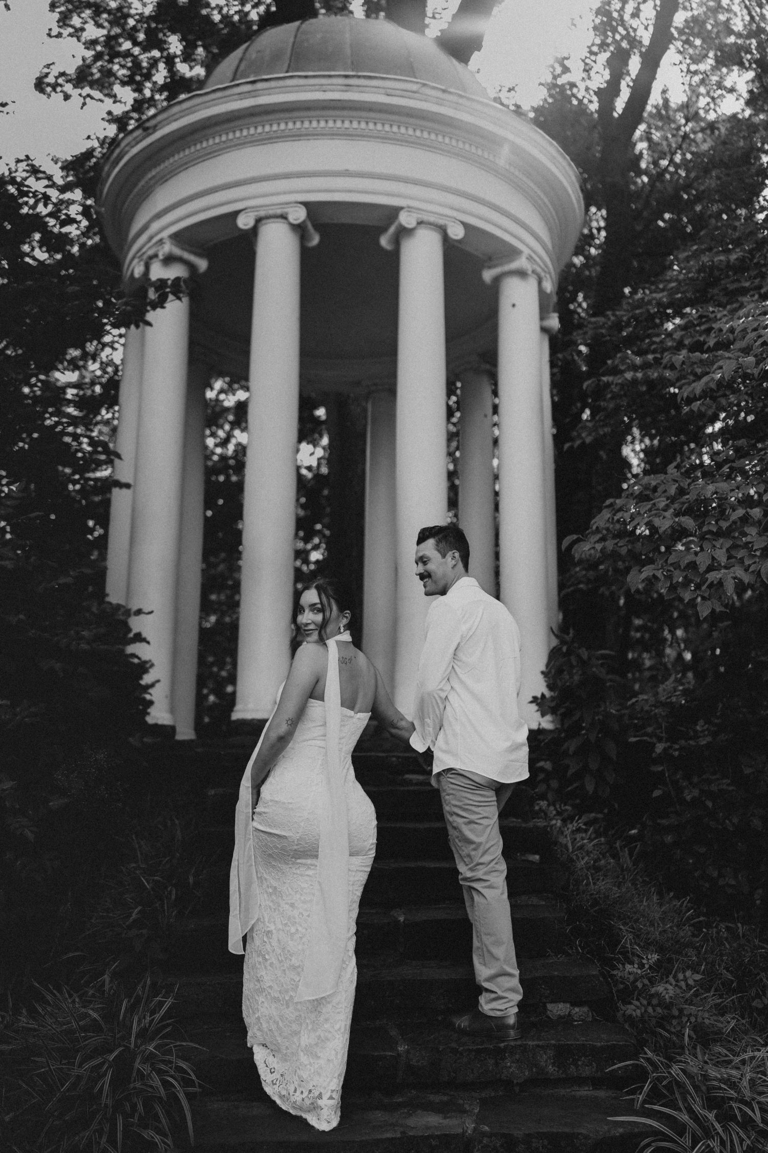 Black and white photo of a bride and groom on stone steps before a classical rotunda with columns.