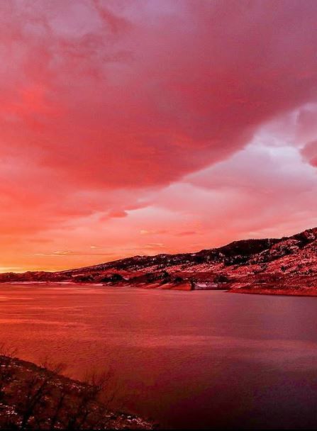 Stunning crimson and pink sunset reflecting over a calm lake with rocky hillside silhouettes.
