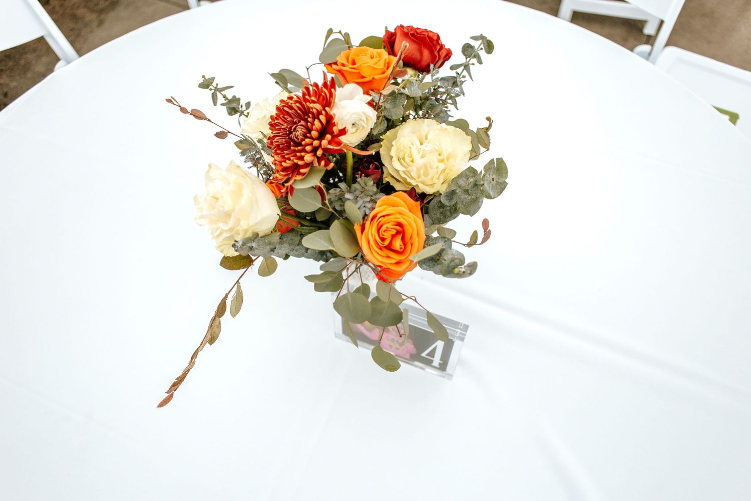 Autumn wedding centerpiece with orange roses, cream flowers, dahlias, and eucalyptus on a white round table.