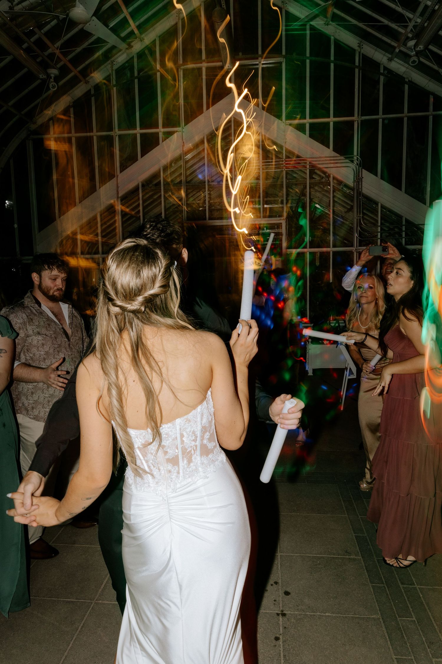 Bride in lace wedding gown holding a sparkler while dancing at a greenhouse wedding.
