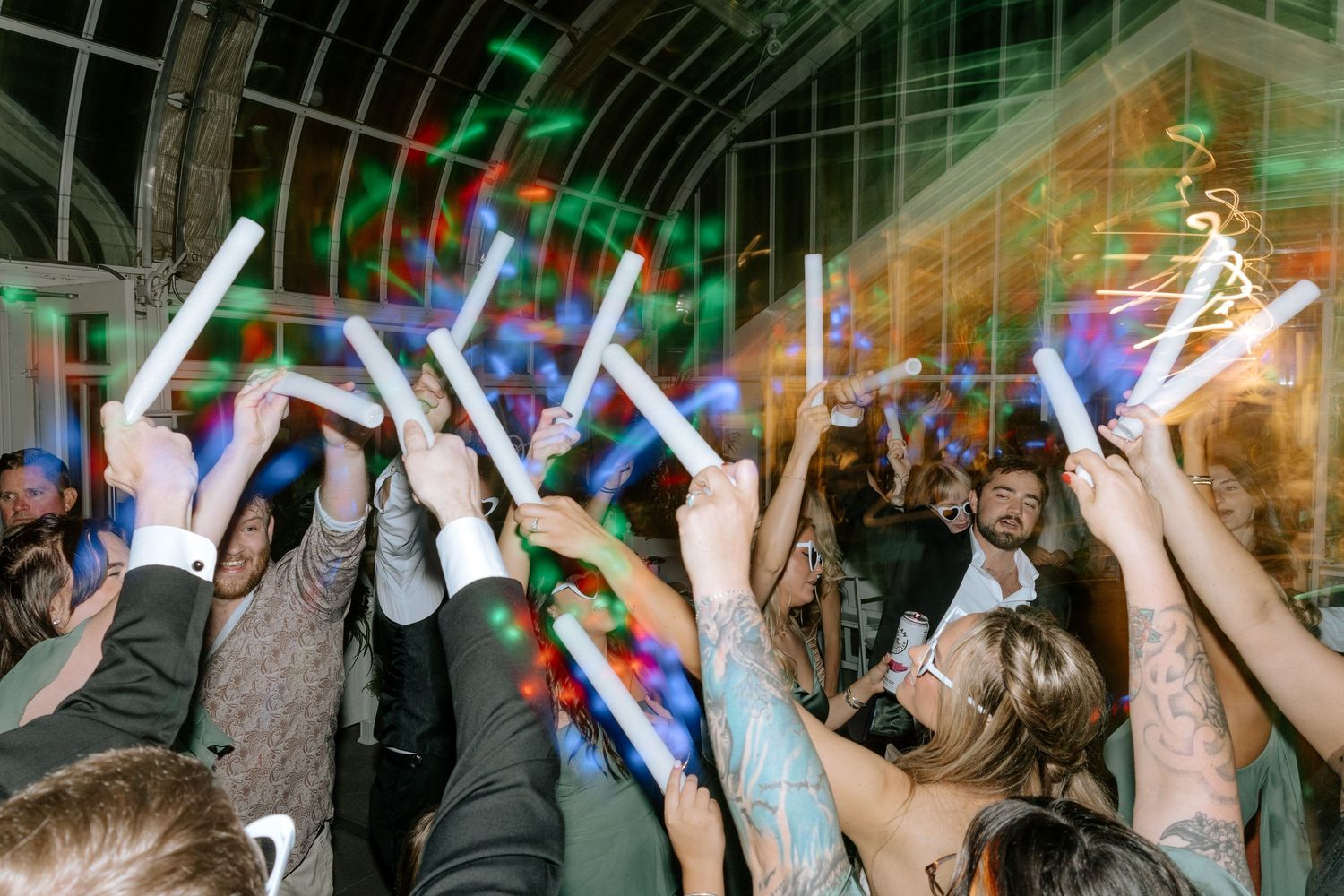 Wedding guests raising glowing foam sticks on a crowded dance floor at a reception.