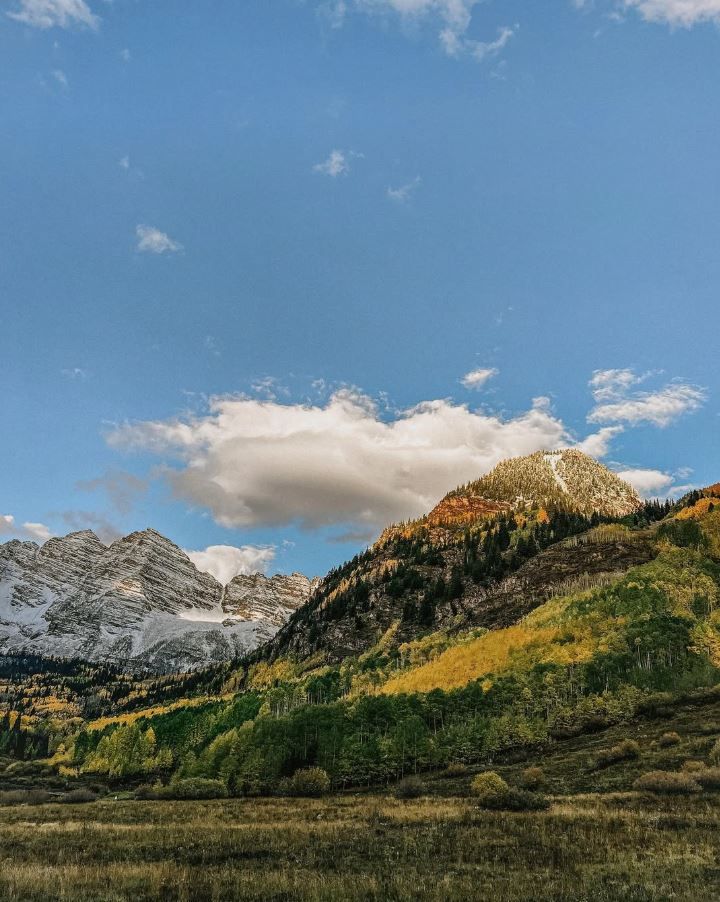 Autumn mountain landscape with snow-capped peaks, colorful foliage, and dramatic clouds in a blue sky.