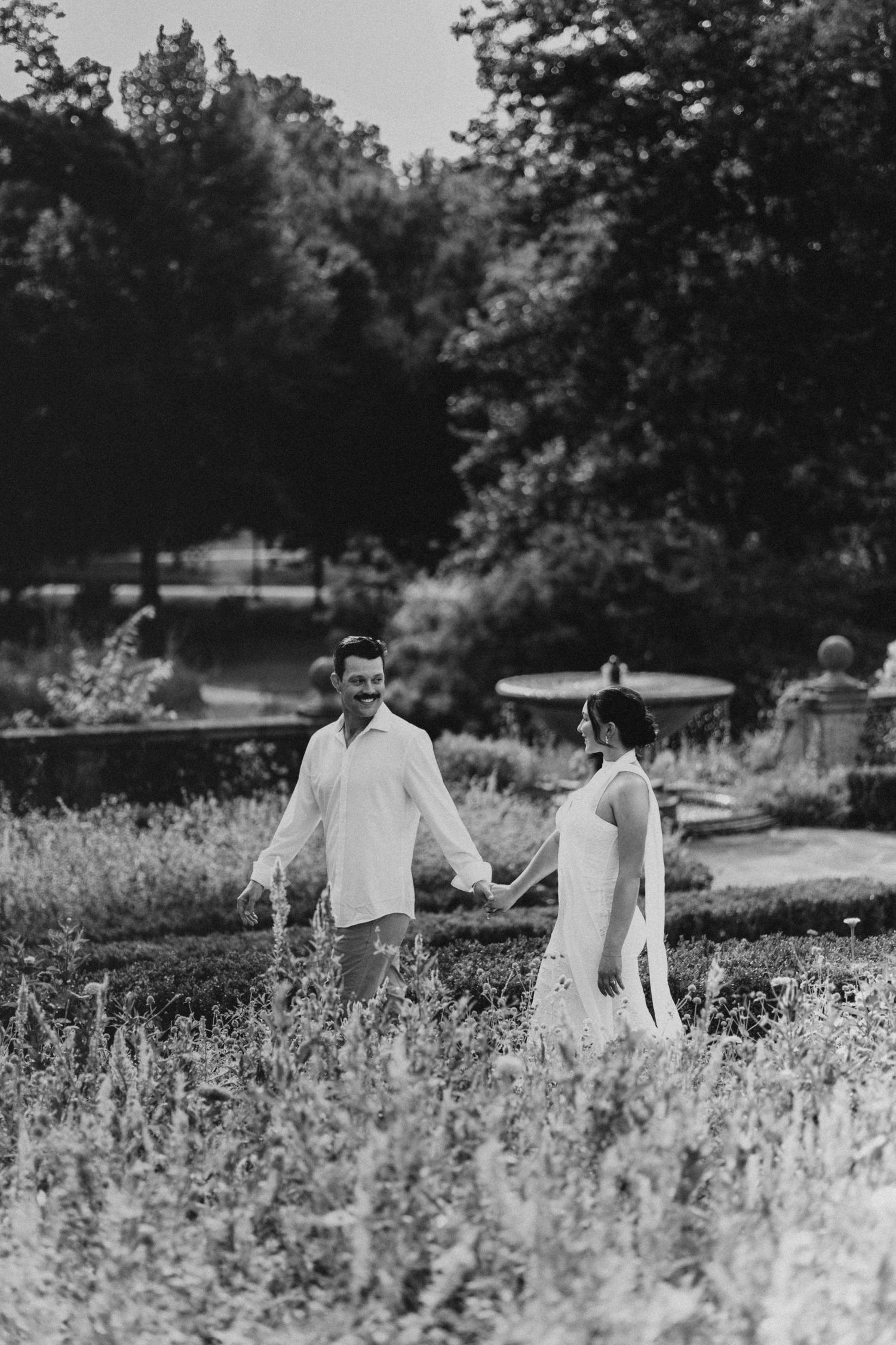 Black and white photo of a couple holding hands walking through a lush garden during their engagement session.