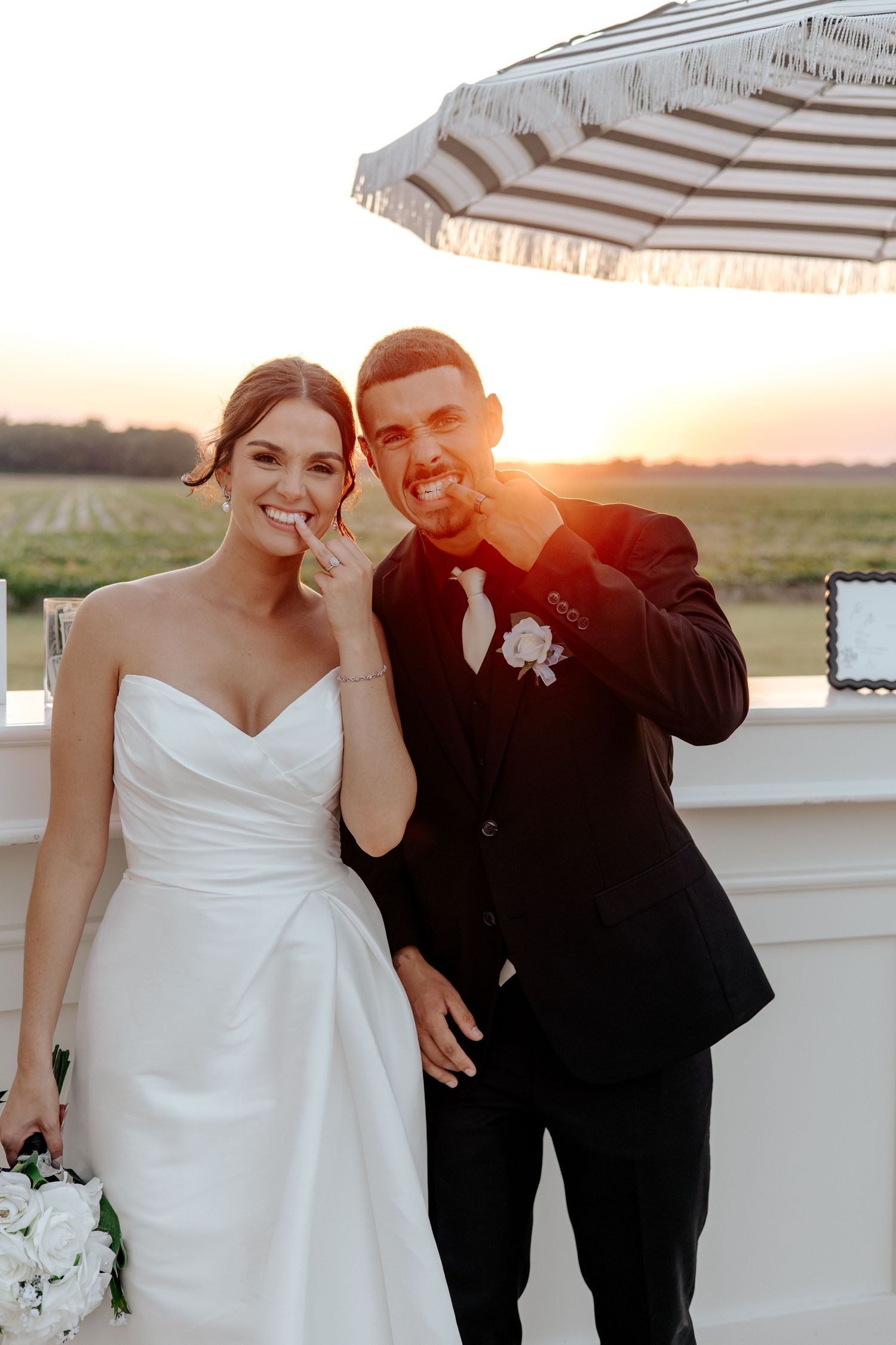 Laughing bride and groom pose together at sunset on a rooftop terrace with striped umbrella.