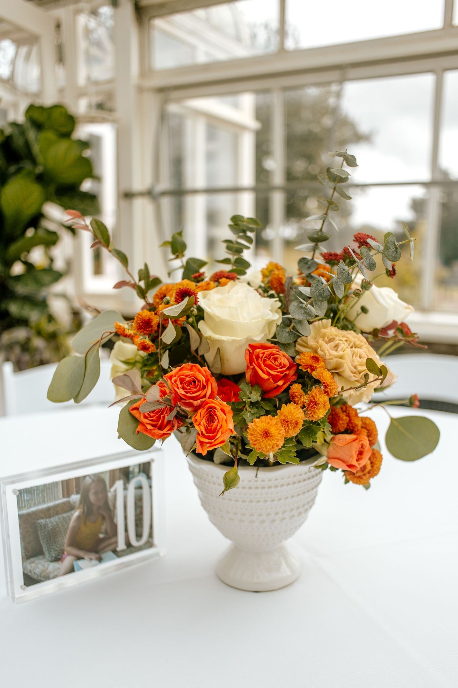 Autumn floral centerpiece with orange and cream roses in white vase on table.