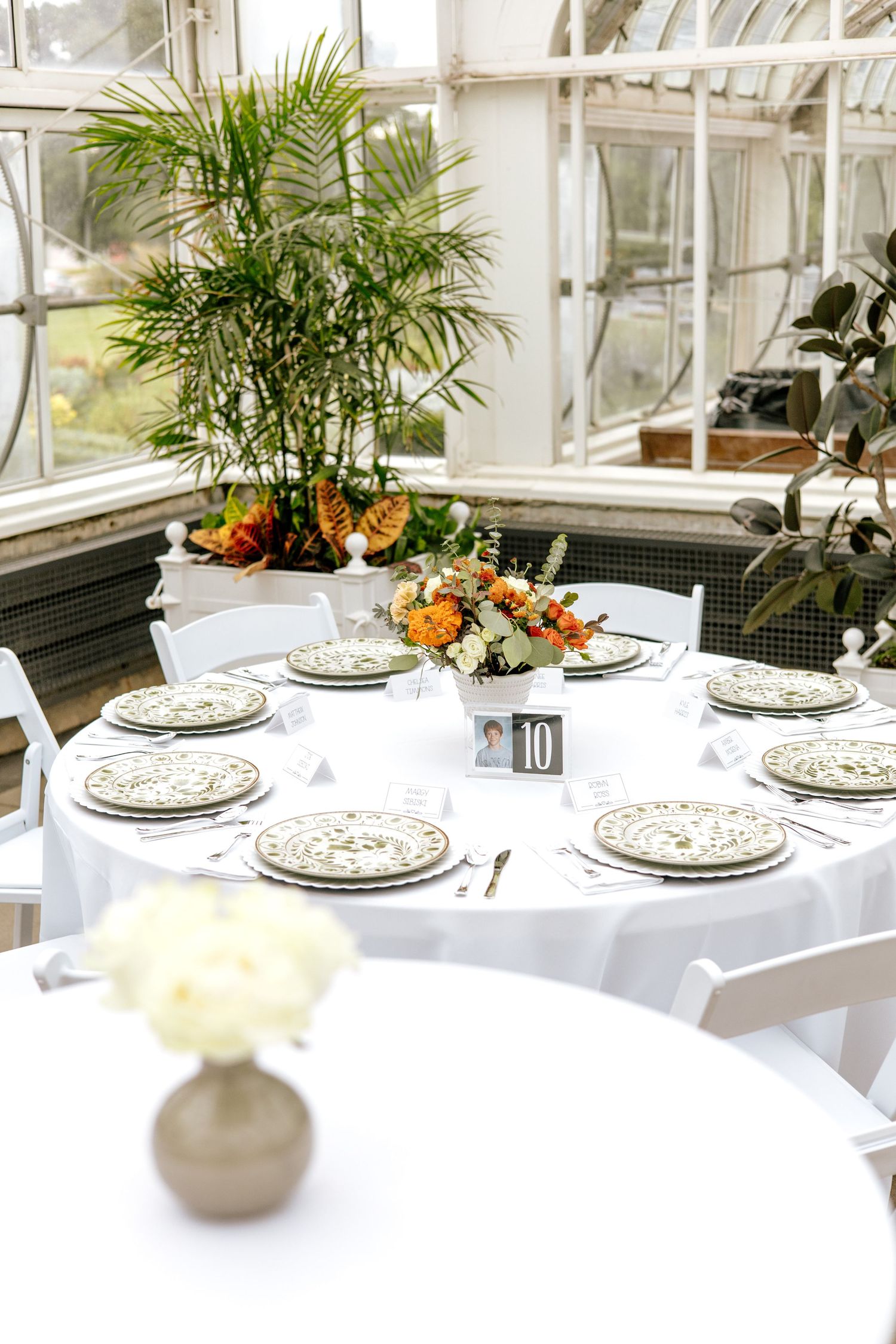 Round wedding reception table set with decorative plates and floral centerpiece, numbered table 10 in a greenhouse setting.