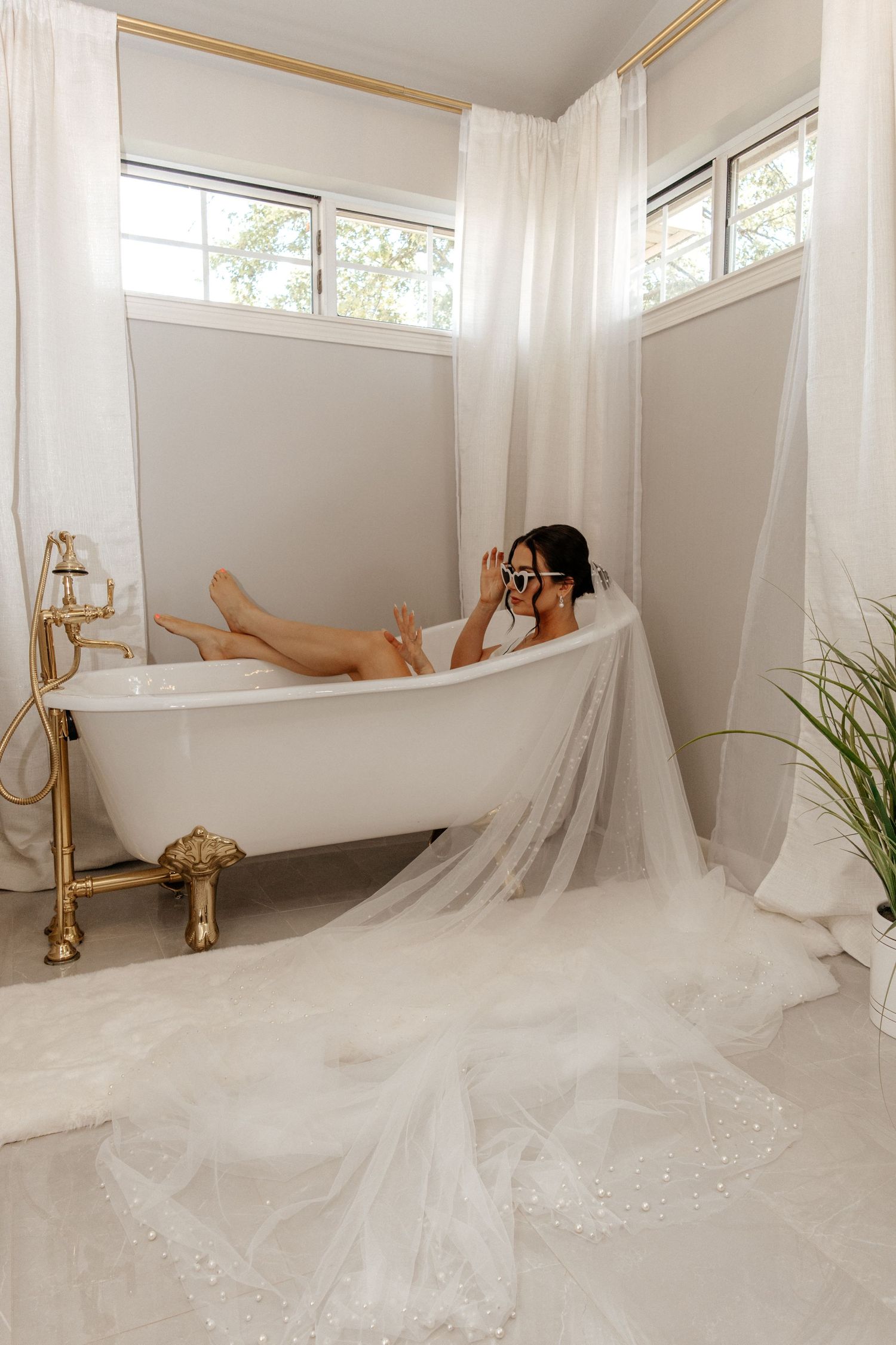 Bride relaxing in a clawfoot bathtub with her white veil draped elegantly over the tub edge.