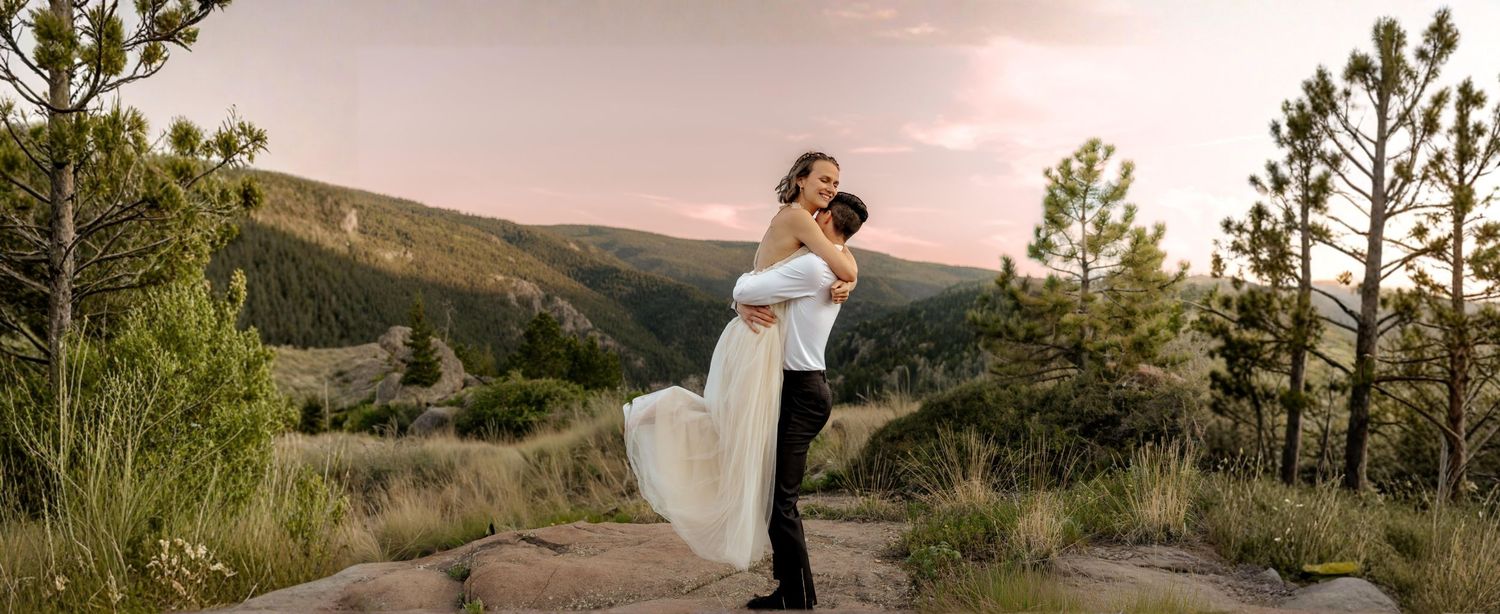 Candid elopement photography featuring a groom lifting his bride against a mountain landscape at dusk
