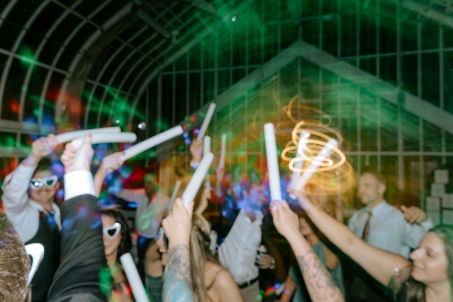 Wedding guests waving glow sticks and sparklers on a lively dance floor at a reception.