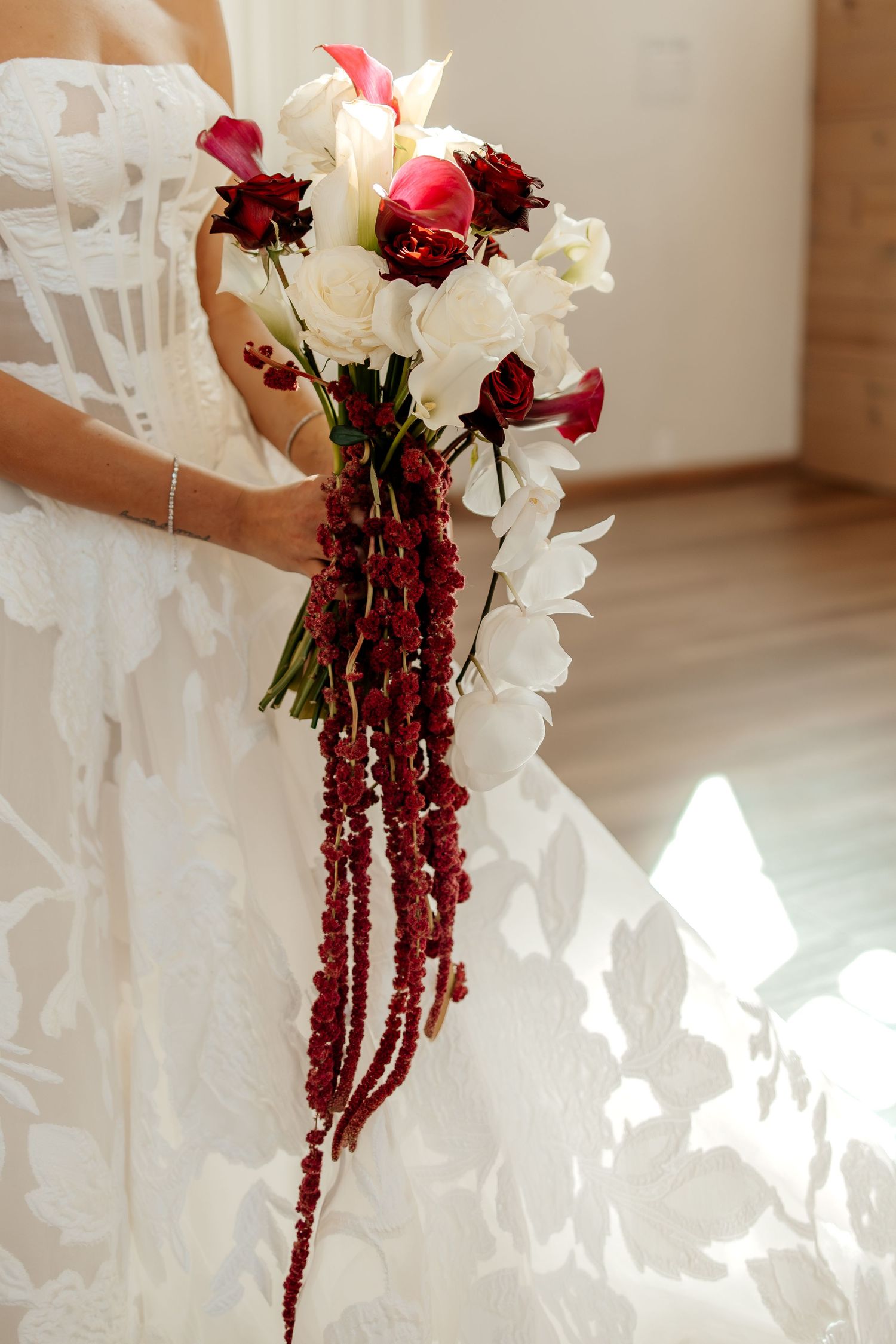 Bride holding a cascading wedding bouquet with white orchids, red roses, and deep red berry strands.