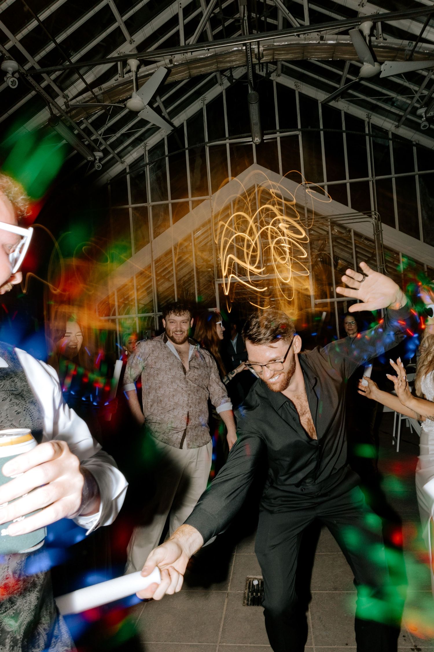 Guests dancing energetically with glow sticks under colorful lights at a wedding reception.