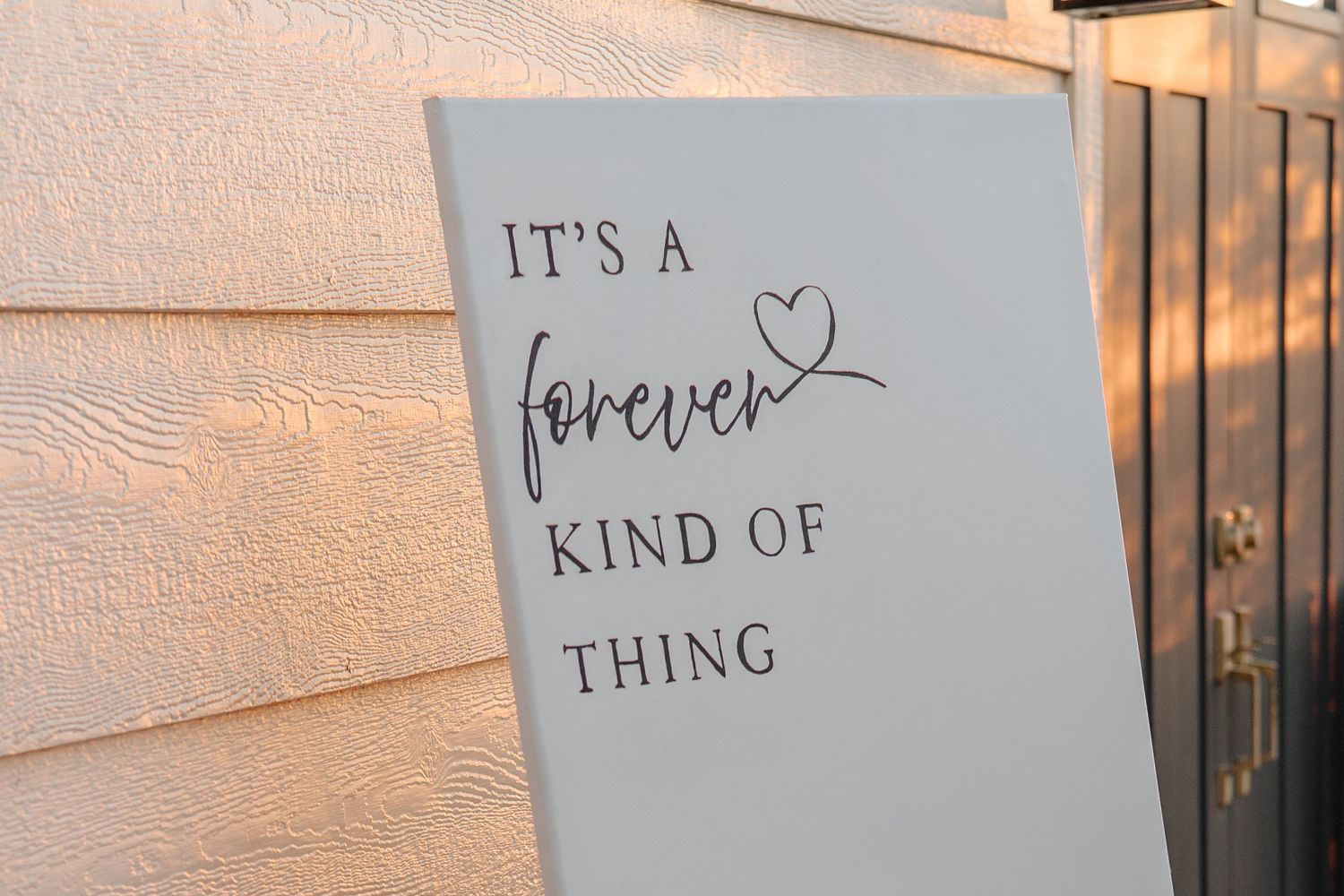 White sign reading It's a Forever Kind of Thing with heart detail, leaning against a wall at golden hour.