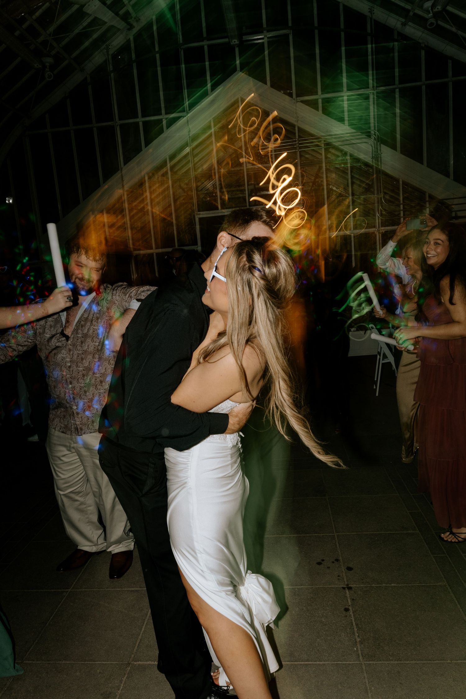Bride in white dress dancing with groom in black suit at a lively wedding reception.