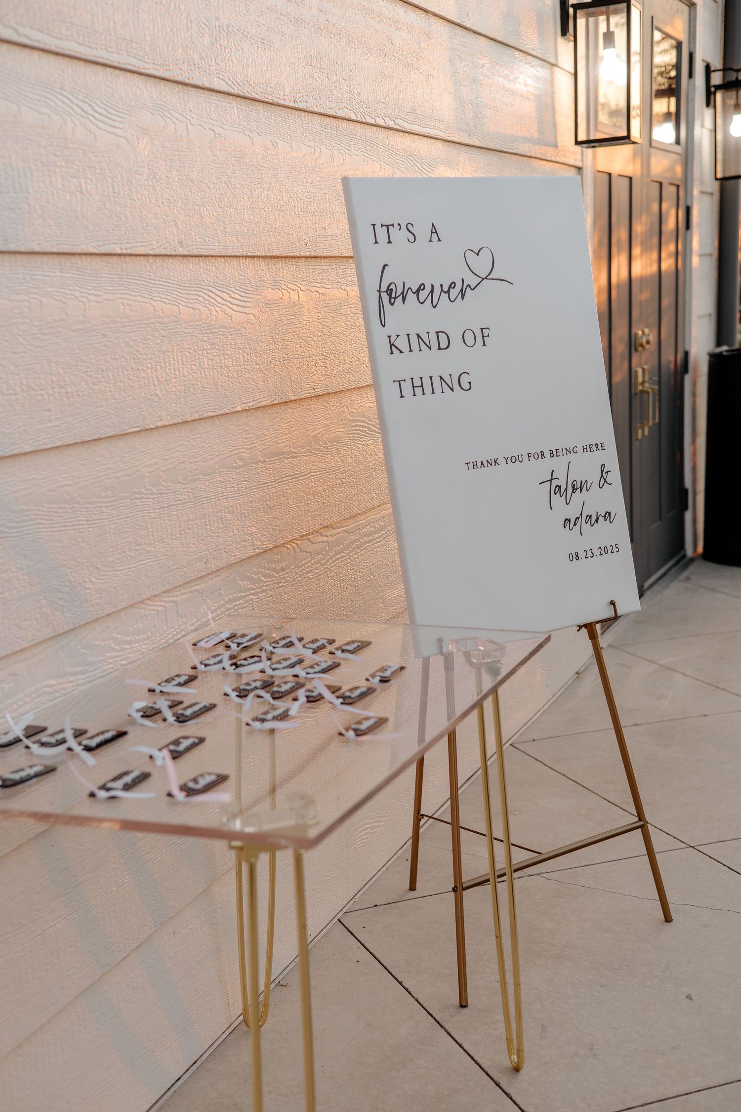 Wedding welcome sign reading It's a Forever Kind of Thing displayed on gold easel with favors.